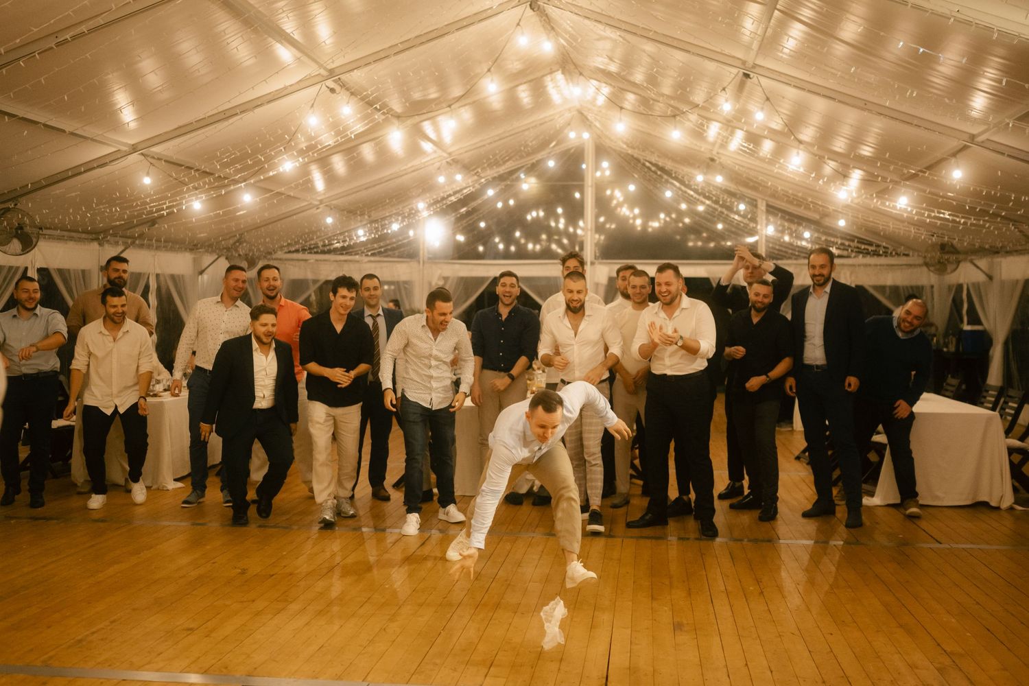 Wedding reception dance floor filled with guests under a tent with string lights creating a warm atmosphere.