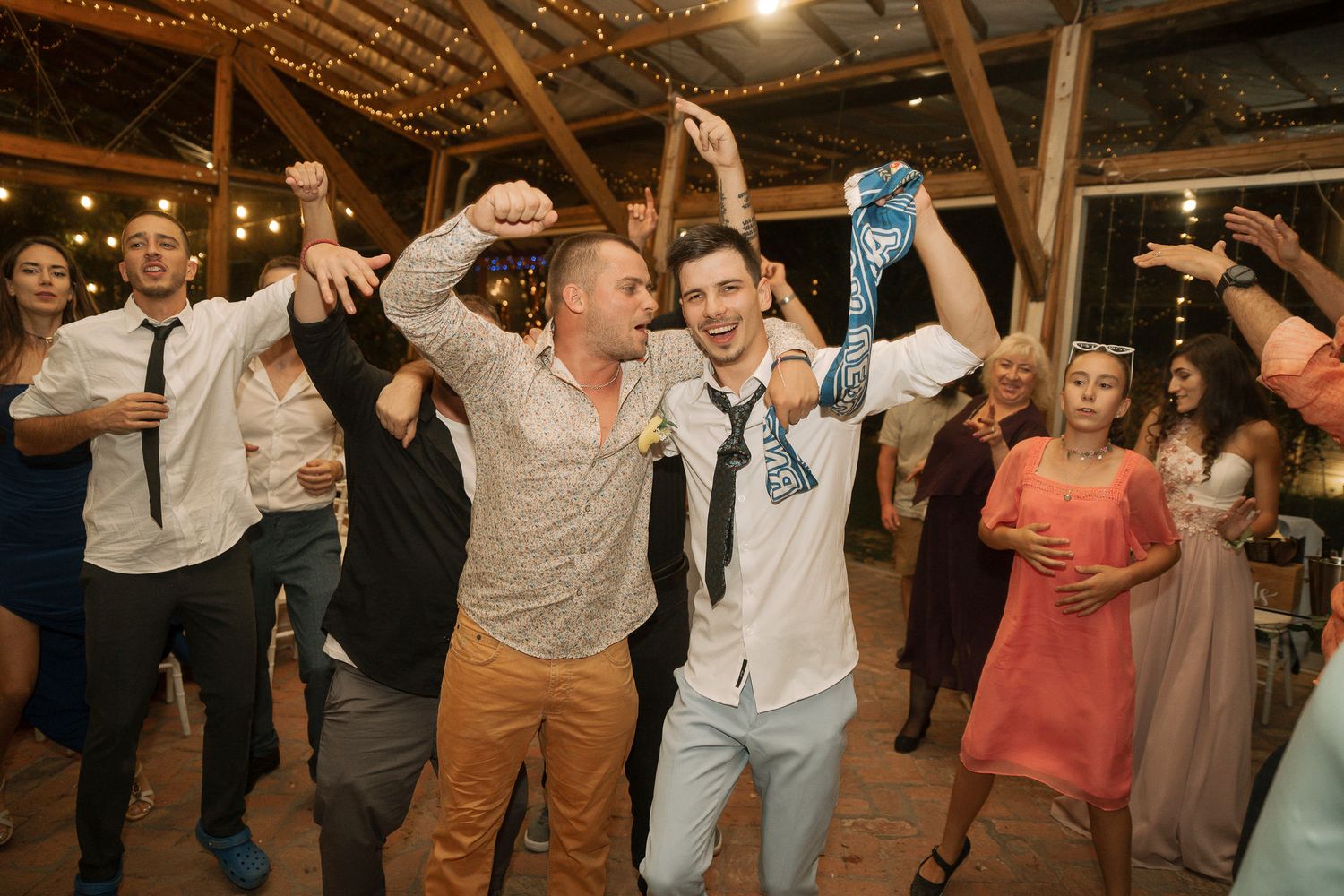 Wedding guests dance together in a rustic barn venue during an energetic reception celebration.