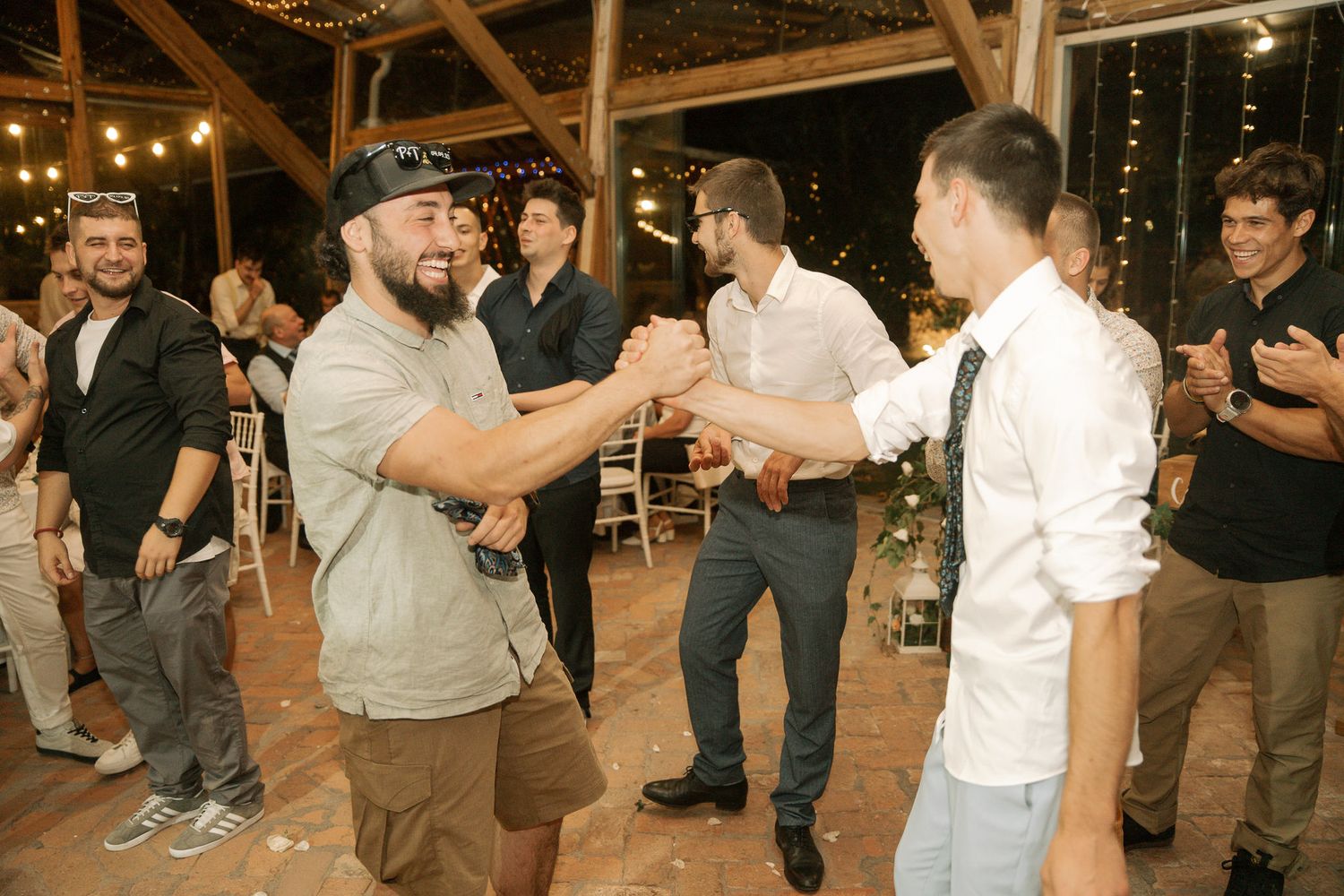 People dancing and socializing at an indoor event with string lights and exposed brick walls in the background.