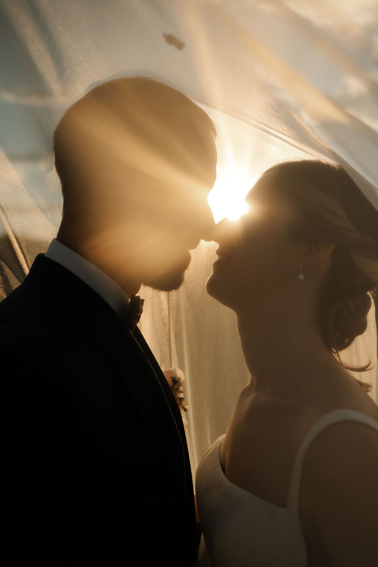 Silhouetted couple in romantic backlit pose against golden sunlight creating atmospheric shadows and warm glow.