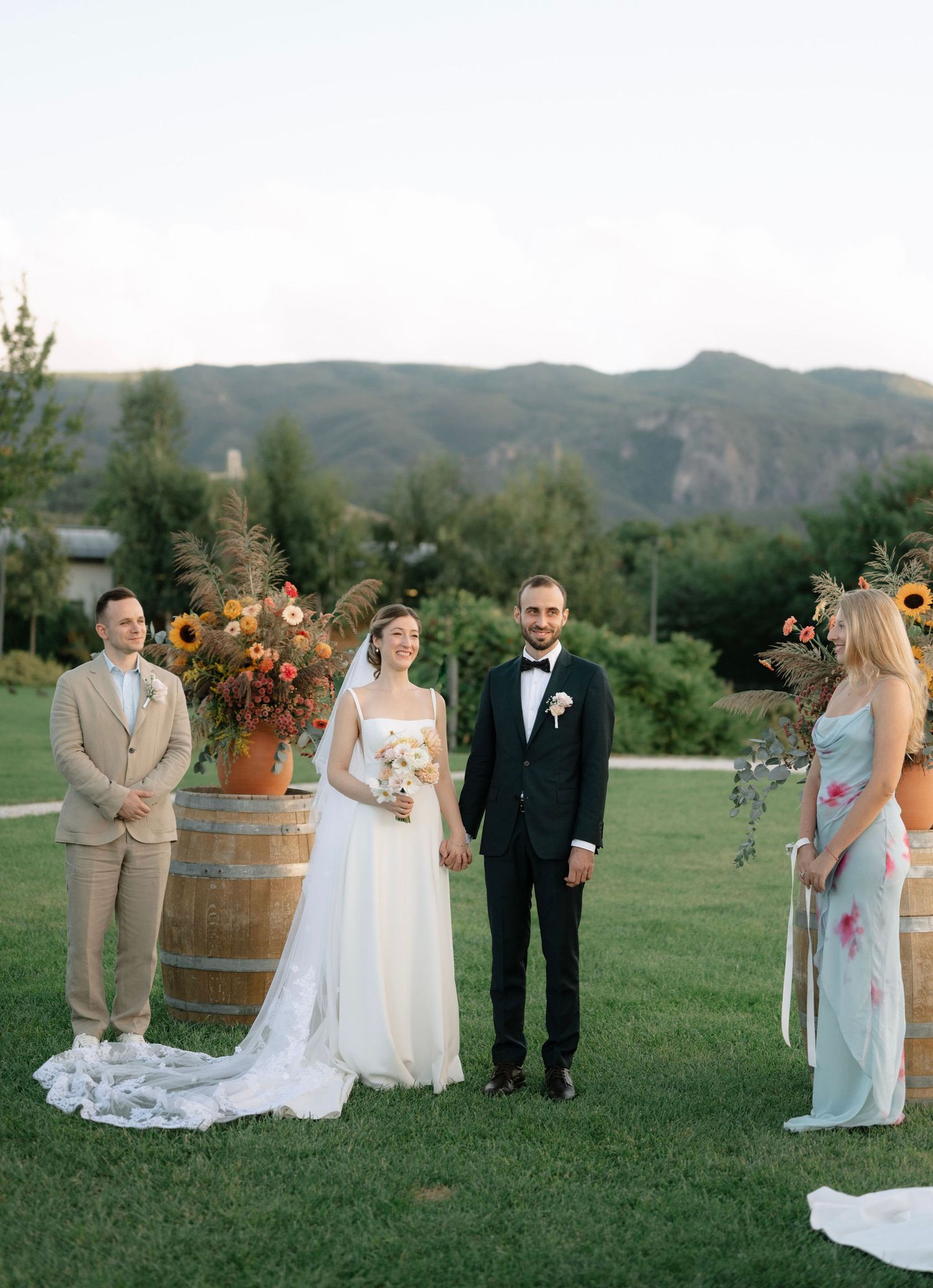 Wedding ceremony setup in a scenic mountain field with rustic wine barrels and sunflower arrangements.