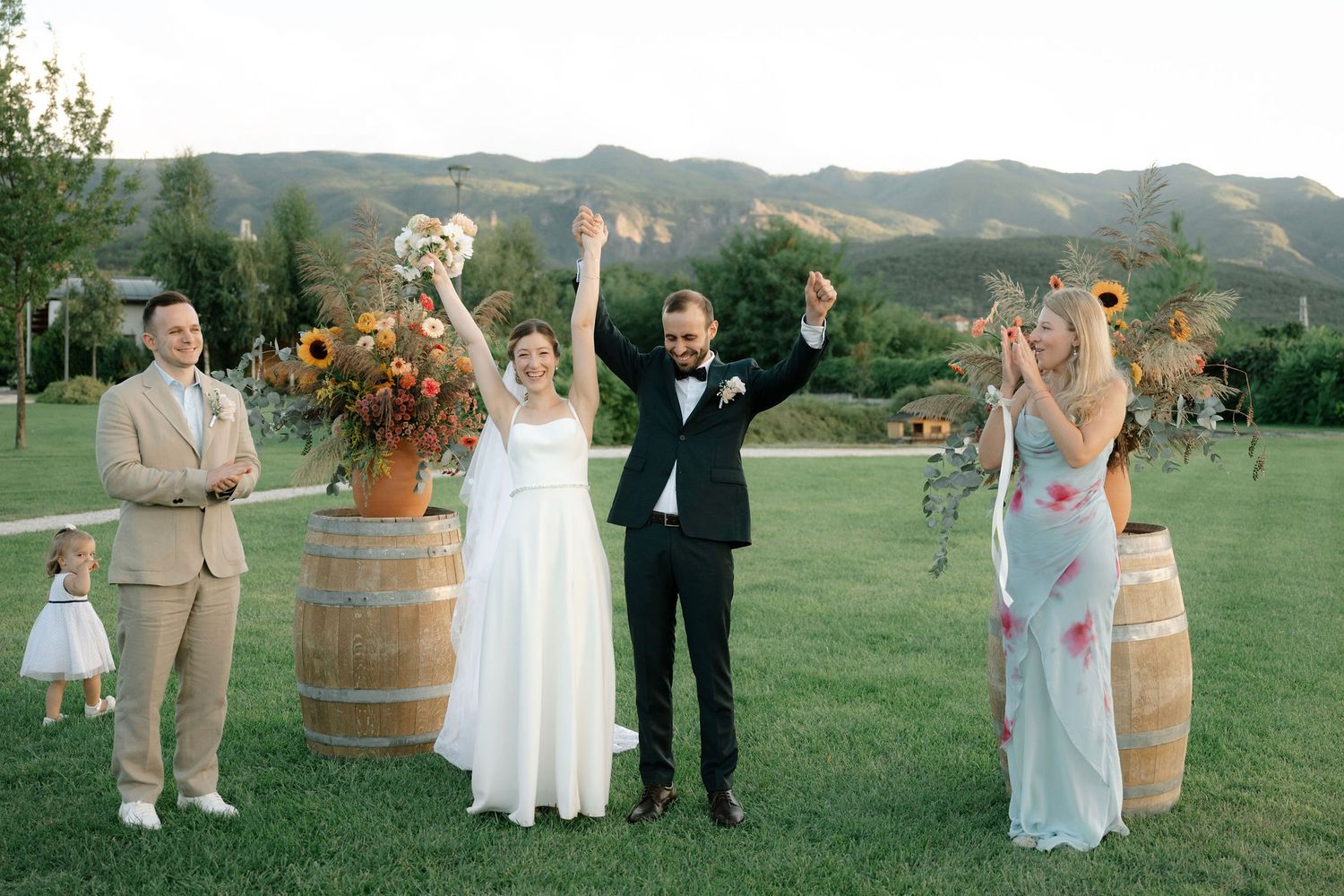 Wedding party celebrates outdoors in a scenic mountain valley setting with wine barrels and rustic decor.
