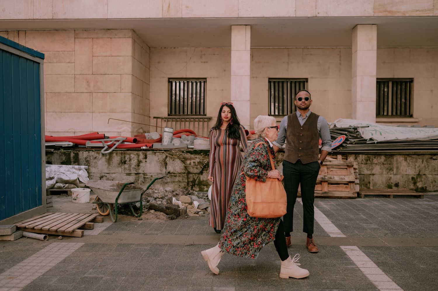 Two women and a bearded man walking together outdoors near a stone building in an urban Middle Eastern setting.
