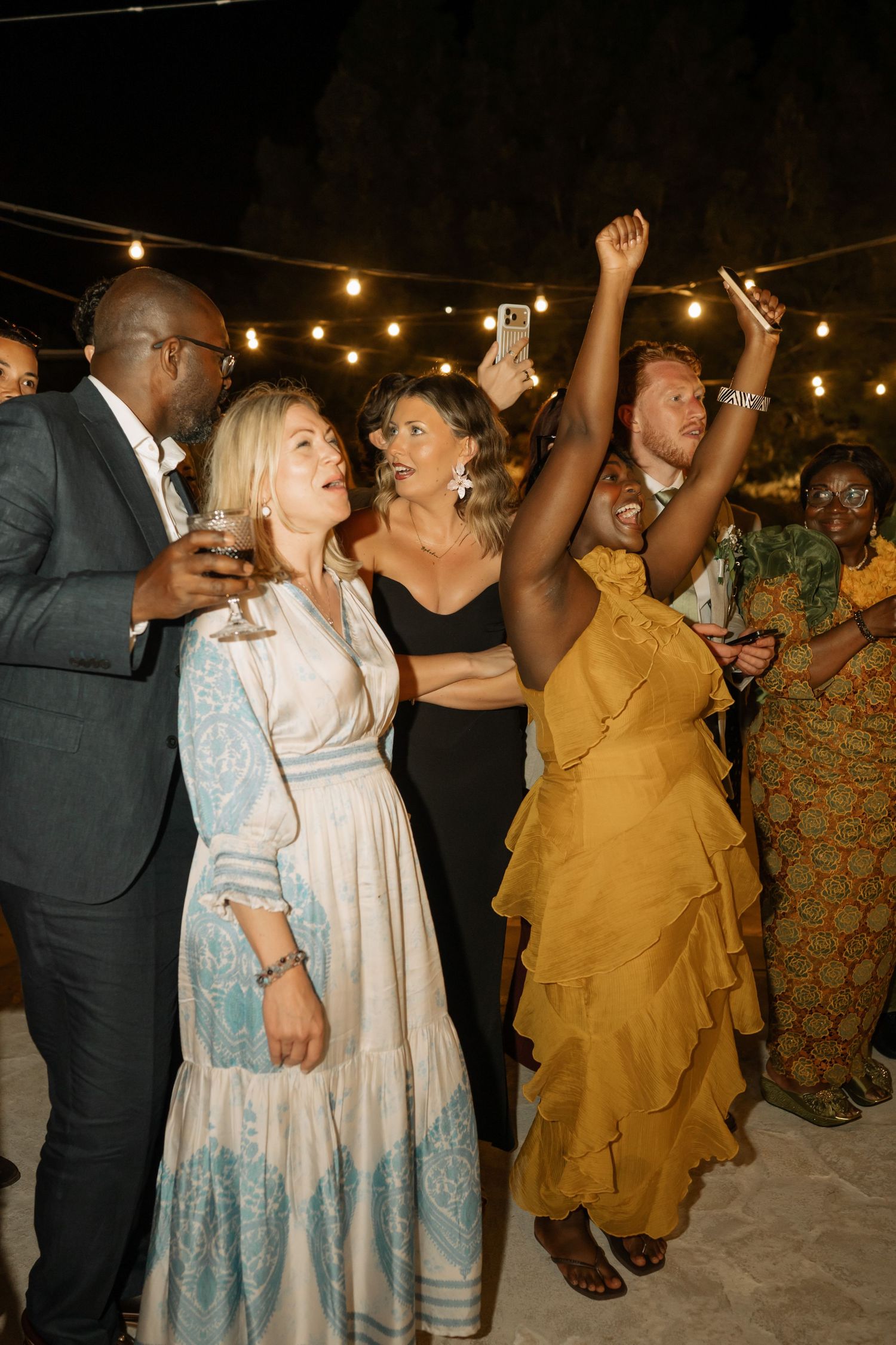 Guests dancing and celebrating at an outdoor evening wedding reception under string lights.