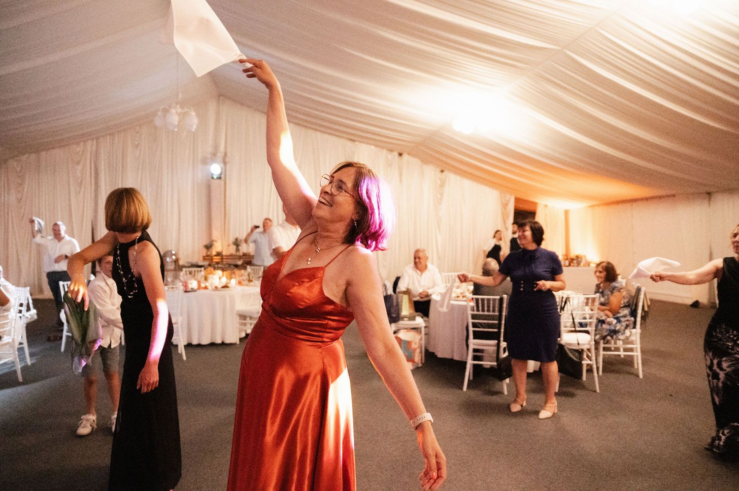 Wedding guests dancing and celebrating on the dance floor in a white draped reception tent.