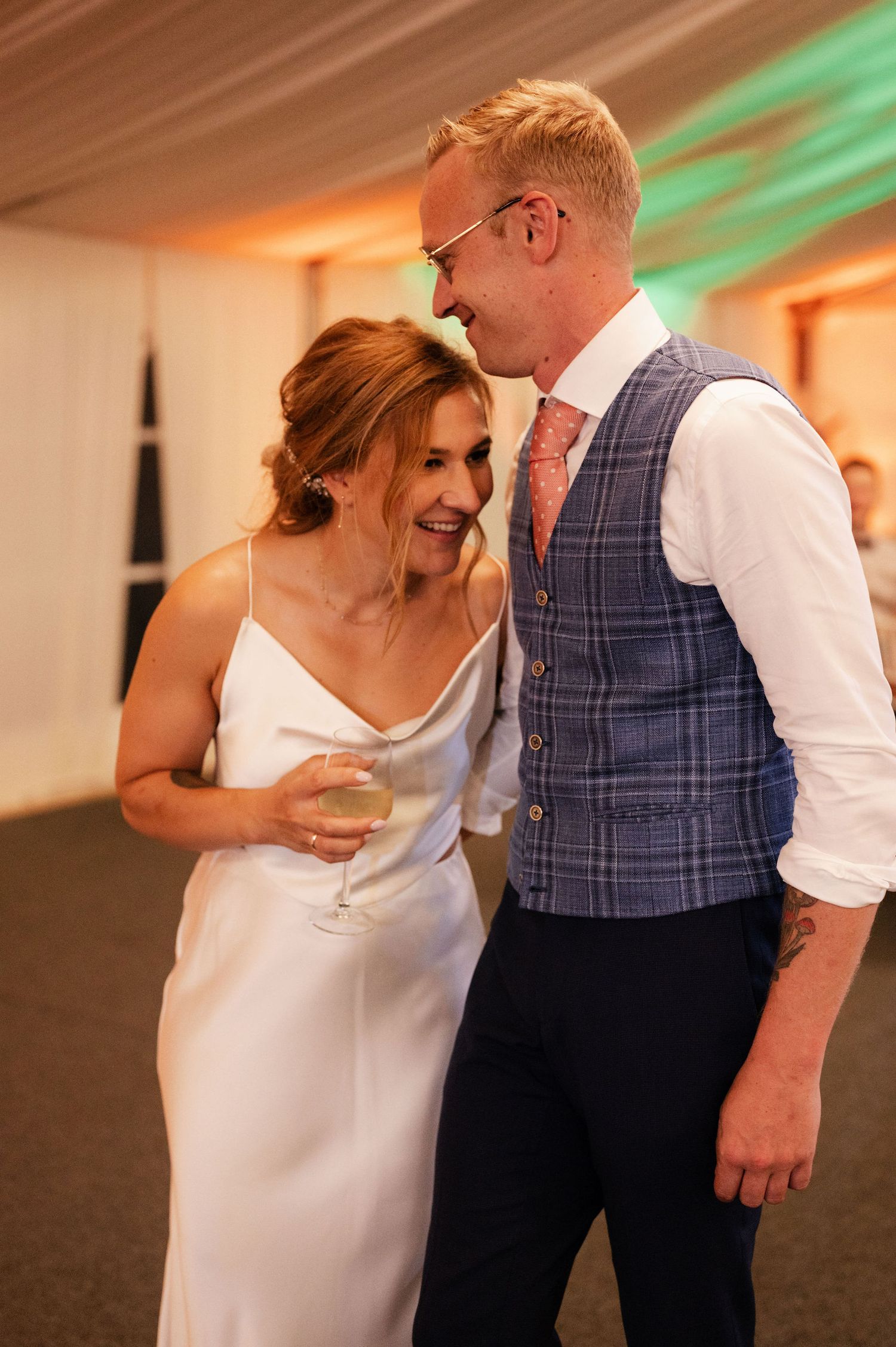 A couple shares an intimate moment on their wedding day, with the bride in white and groom in a plaid vest.