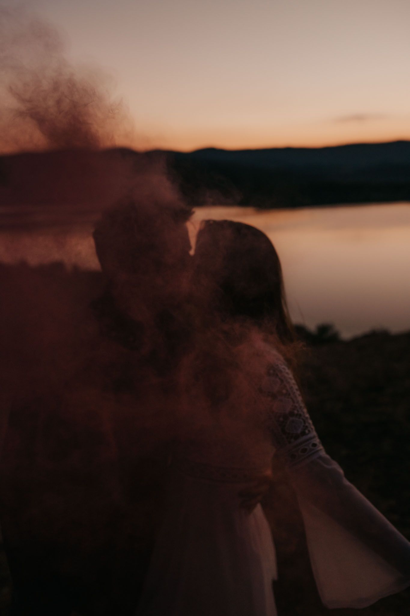 Red smoke billows around figures on a cliff edge during golden hour.