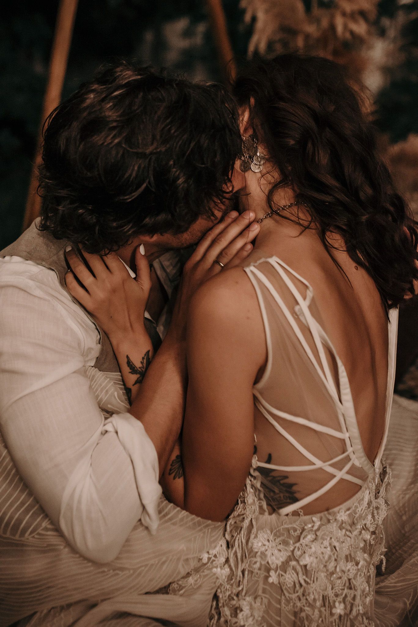 Romantic couple sharing an intimate moment at sunset, with bride wearing strappy back wedding dress in warm lighting.