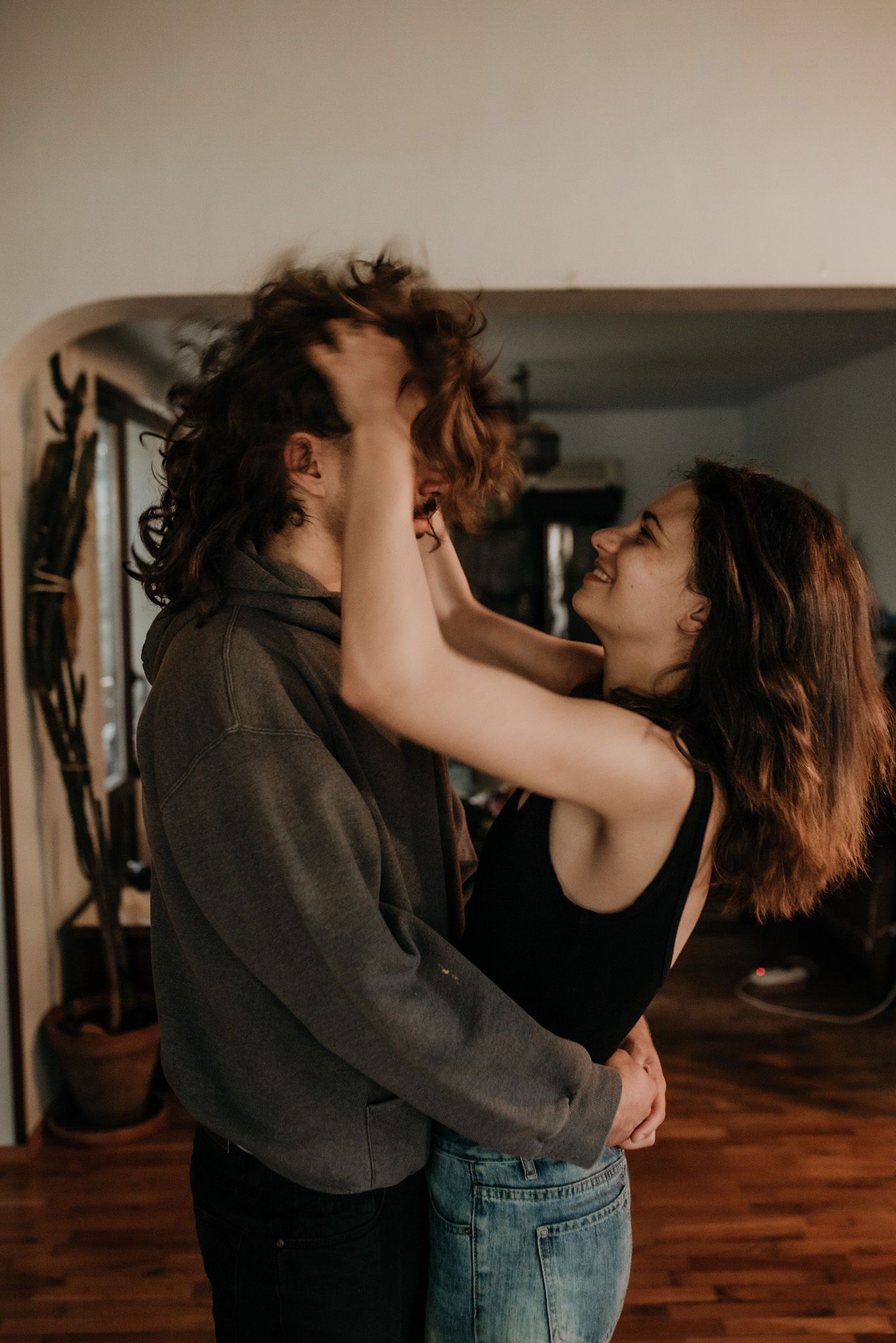 A couple embraces intimately while dancing together in a dimly lit room with wooden floors.