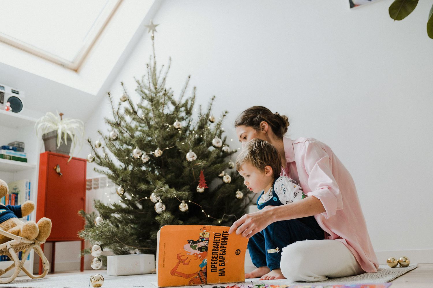 A person in pink sits on a couch with a laptop while working from home near a decorated Christmas tree.
