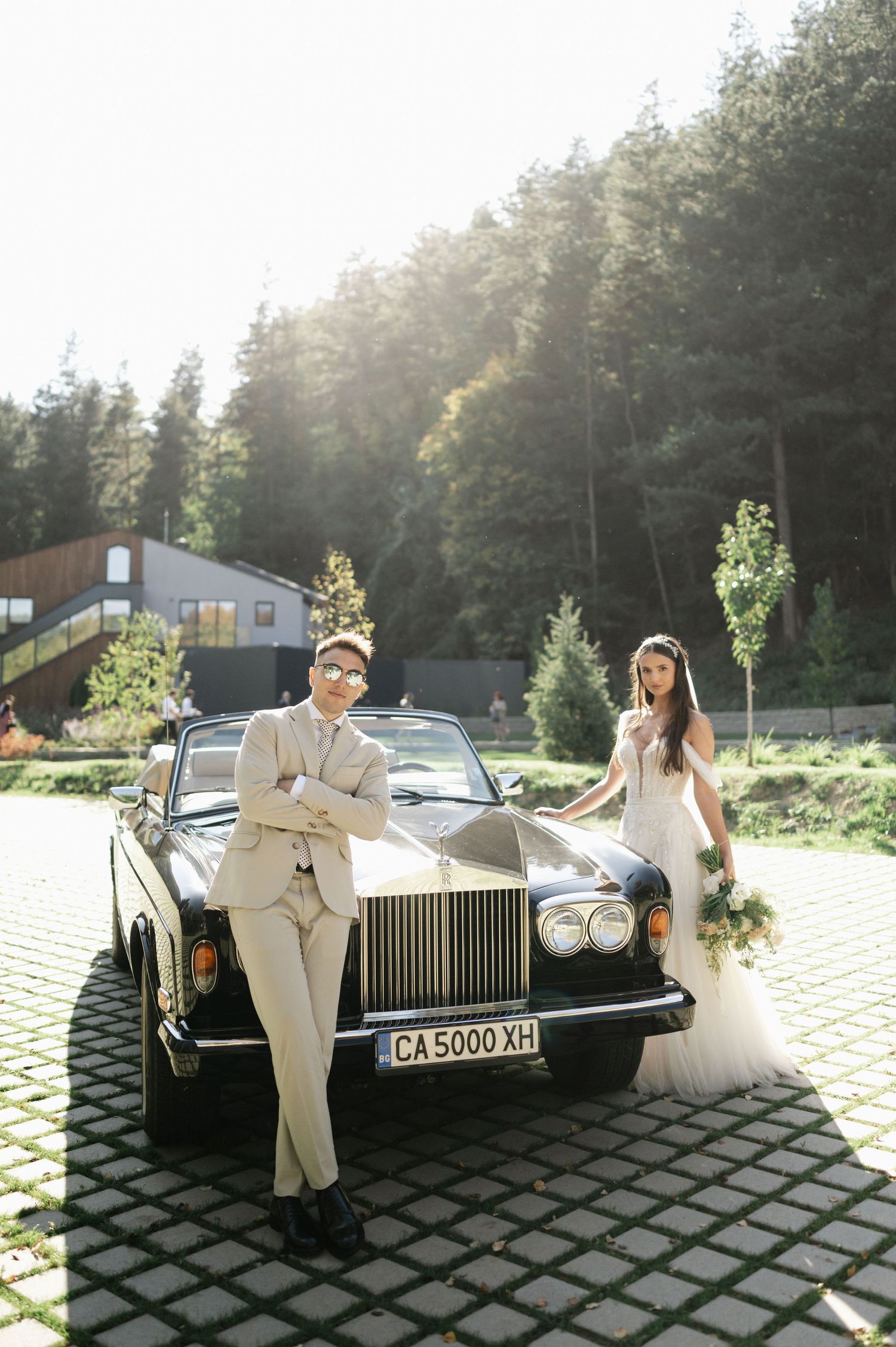 Elegant wedding scene with classic Rolls-Royce parked on patterned stone pavement.