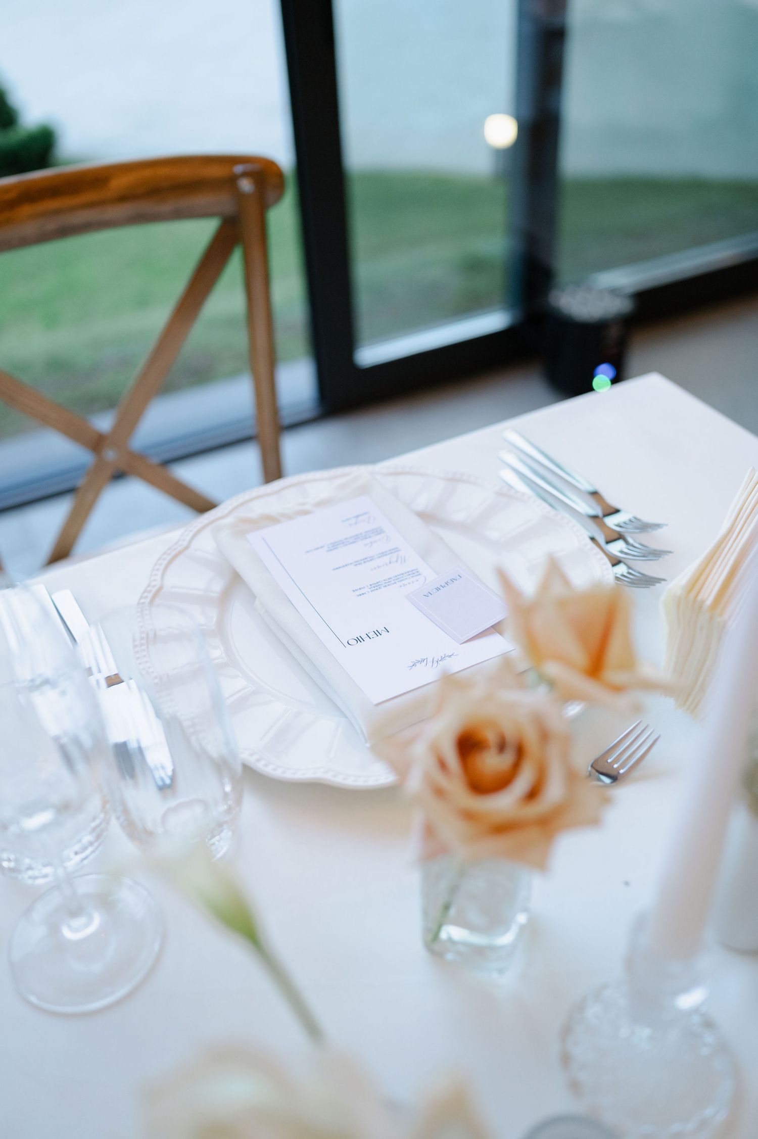 Intimate wedding place setting with delicate peach rose and crystal glassware.