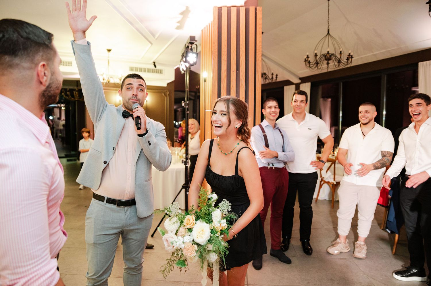 Guests celebrate with raised arms during a lively moment at an indoor reception.