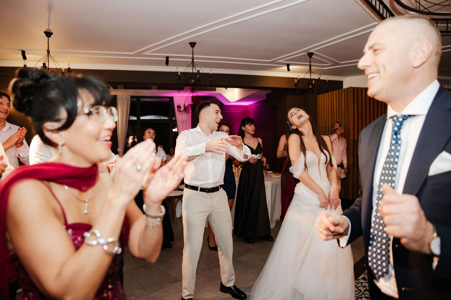 Wedding guests dancing and celebrating on a patterned dance floor with pink accent lighting.