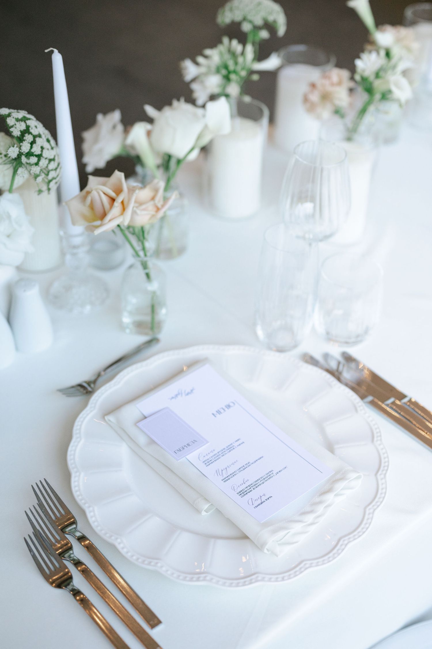 Close-up of minimalist wedding table decor featuring white linens and delicate floral arrangements.