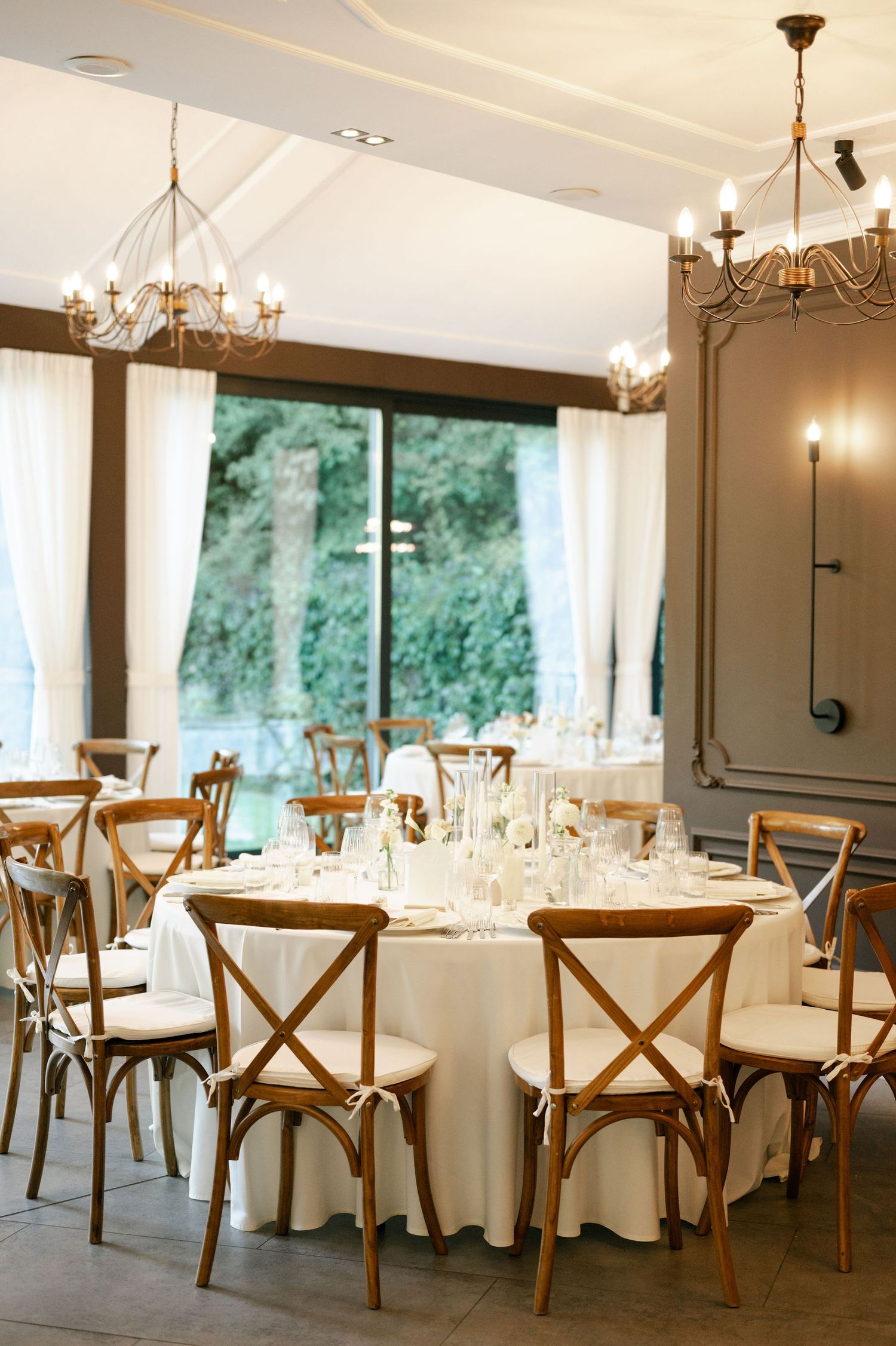 Upscale dining room featuring farmhouse chairs, white tablecloths and panoramic windows with forest views.