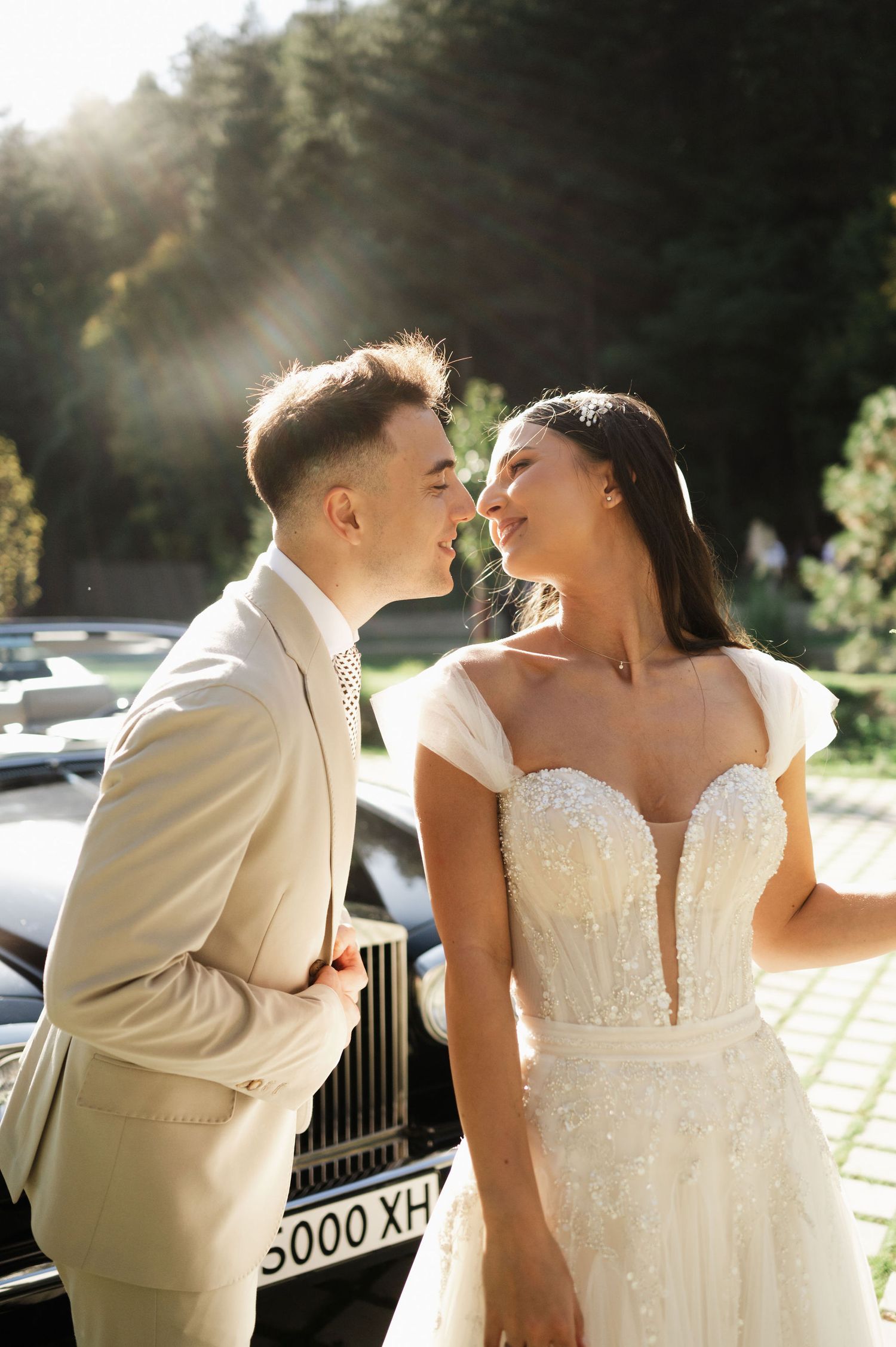 A tender wedding moment photographed against a classic car backdrop in warm sunlight.