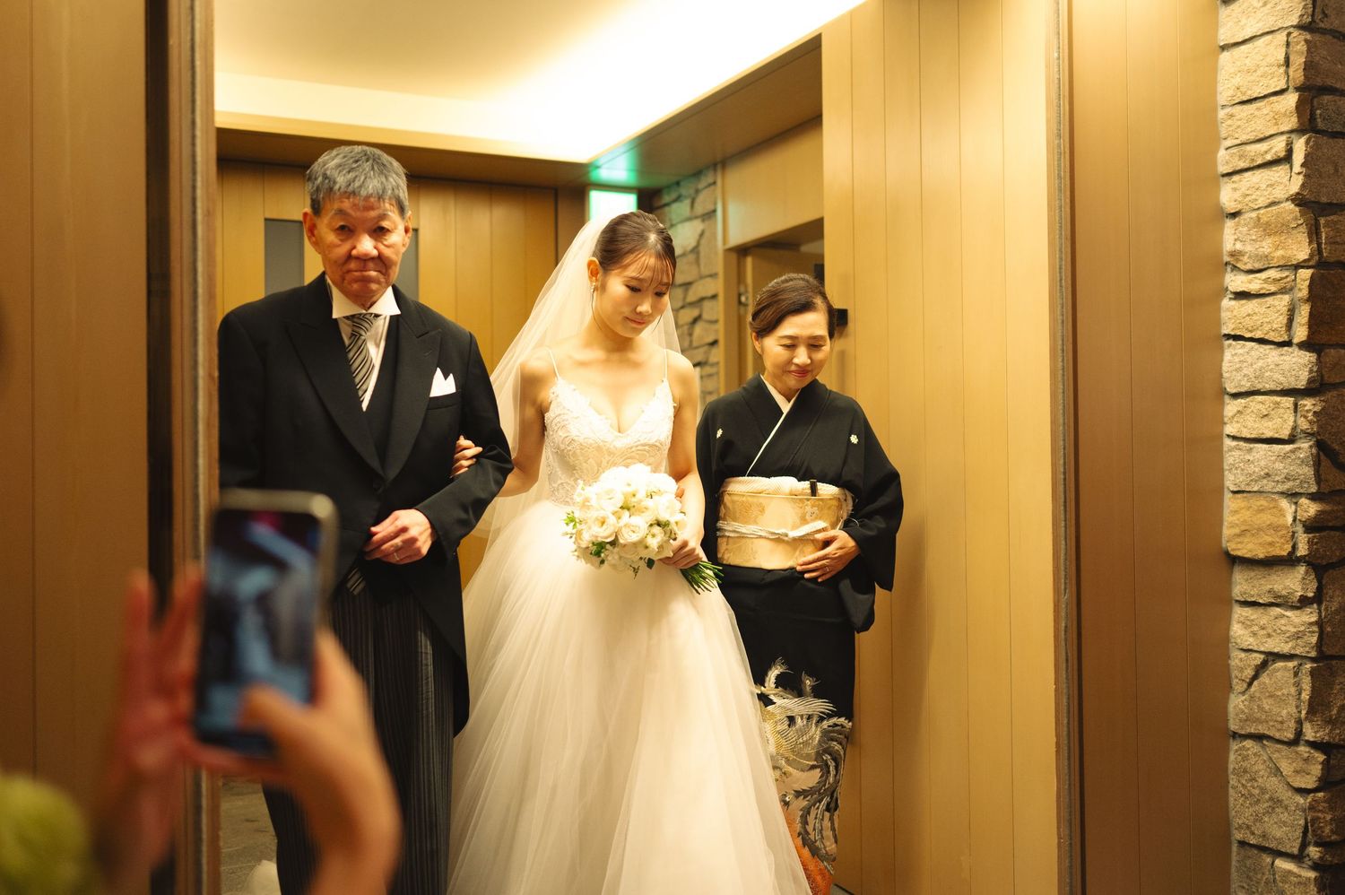 Wedding party members gather in a hallway with stone accent walls and modern lighting.