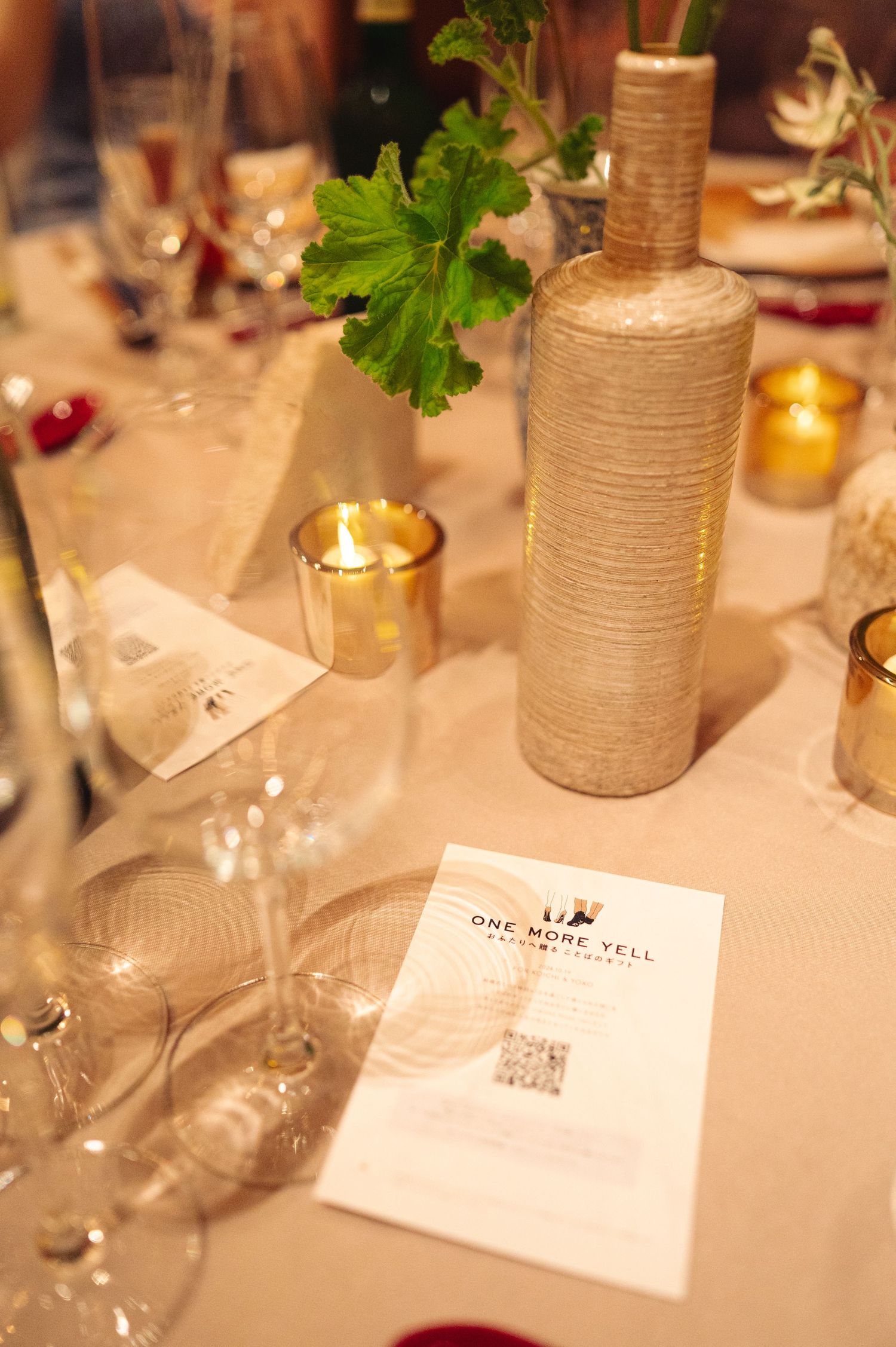Table decorations featuring wrapped vases, menu cards and candlelight on white linens.