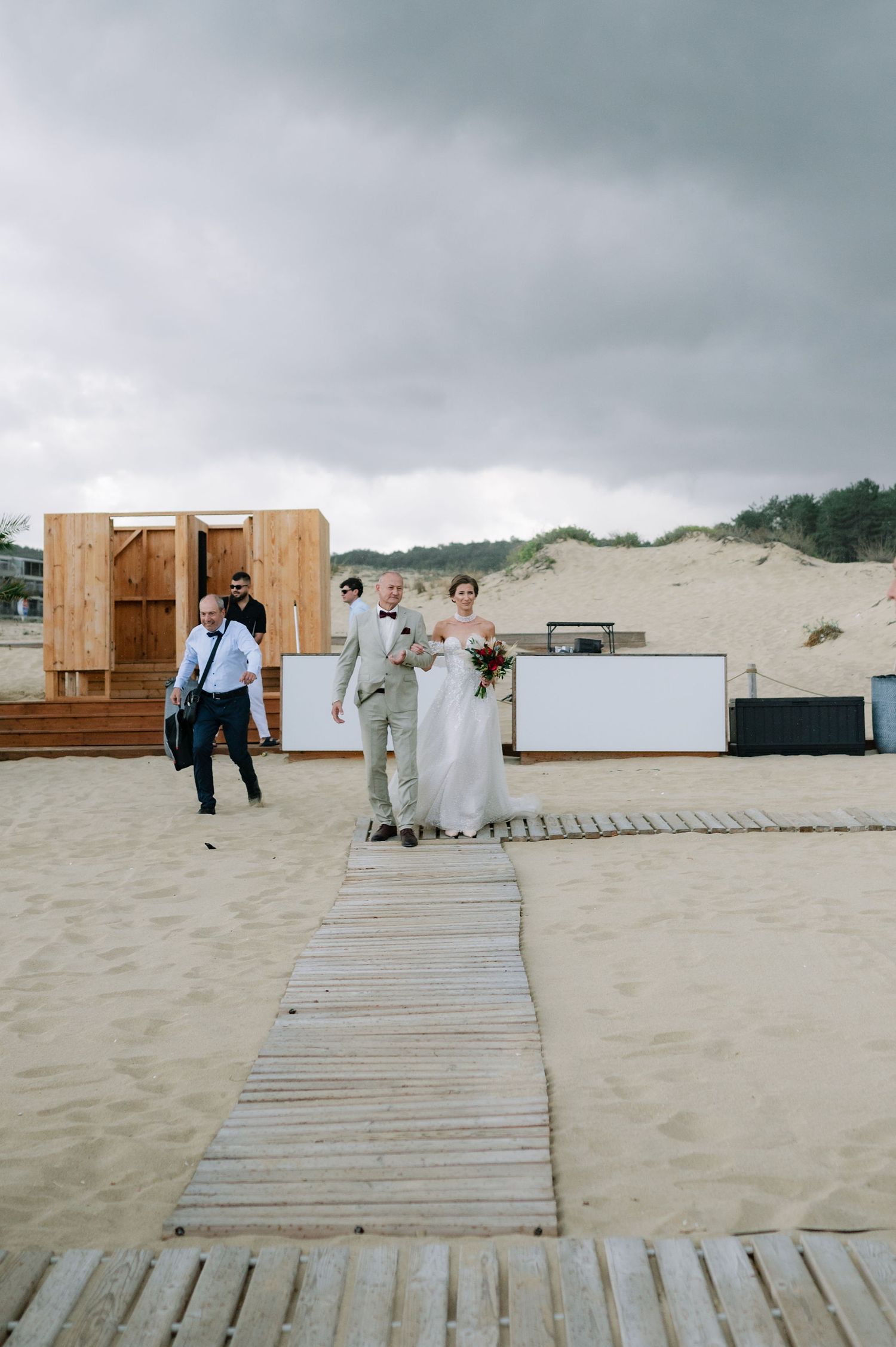 Wooden beach boardwalk leads to rustic wooden structures for outdoor wedding ceremony.