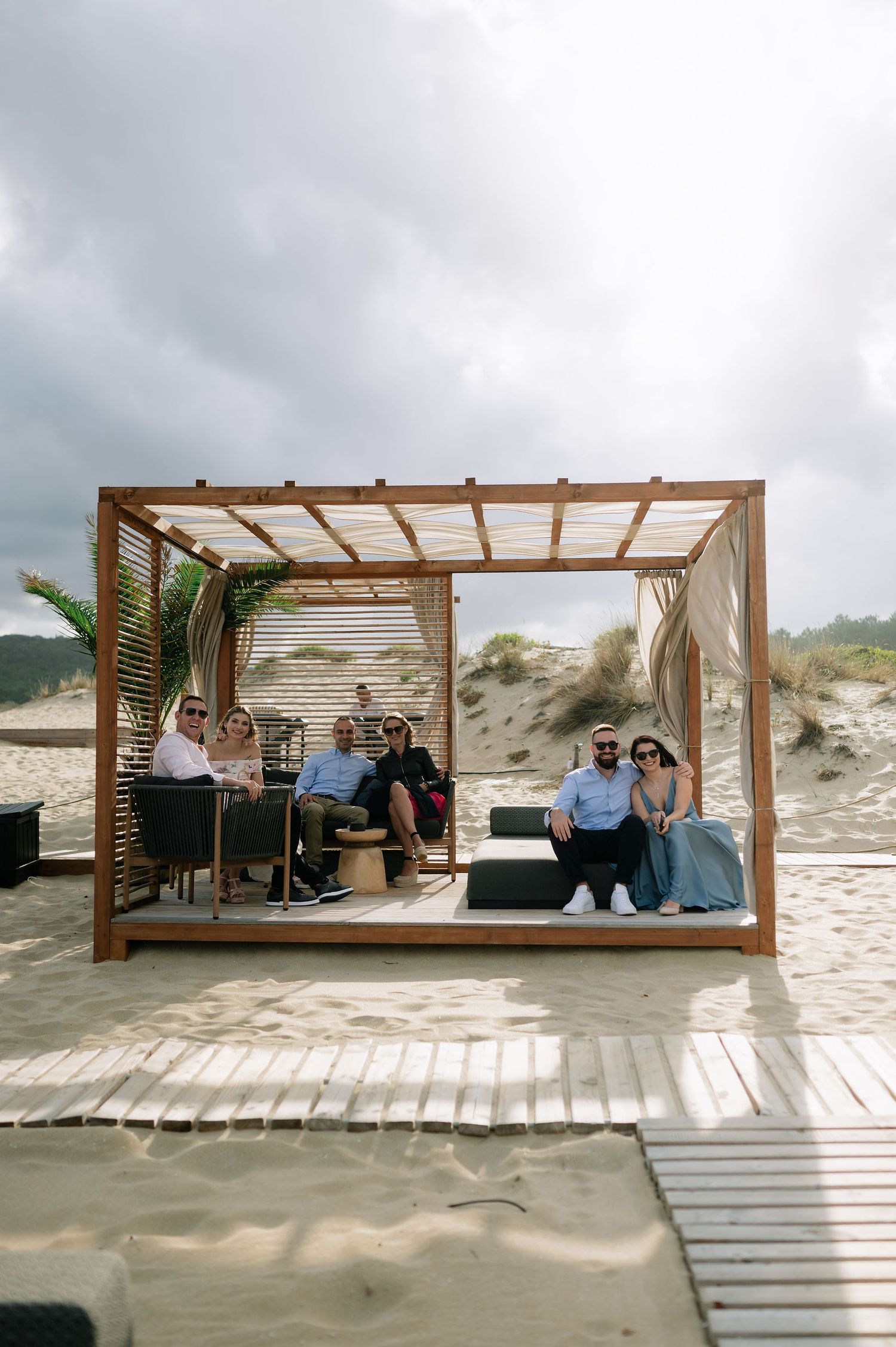 Wooden pergolas with seating areas line a beachfront boardwalk.
