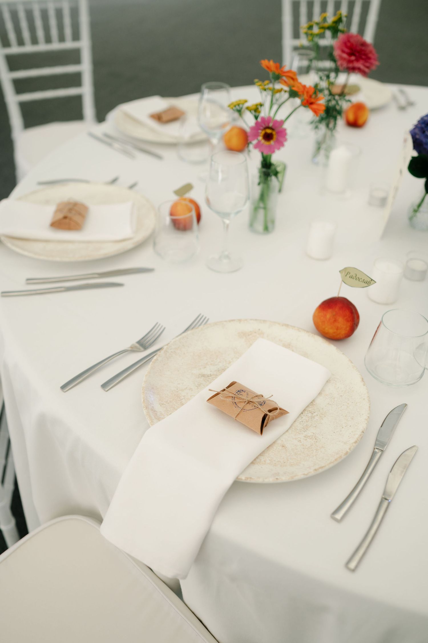 Place settings with white linens, silverware and small floral accents on round reception tables.