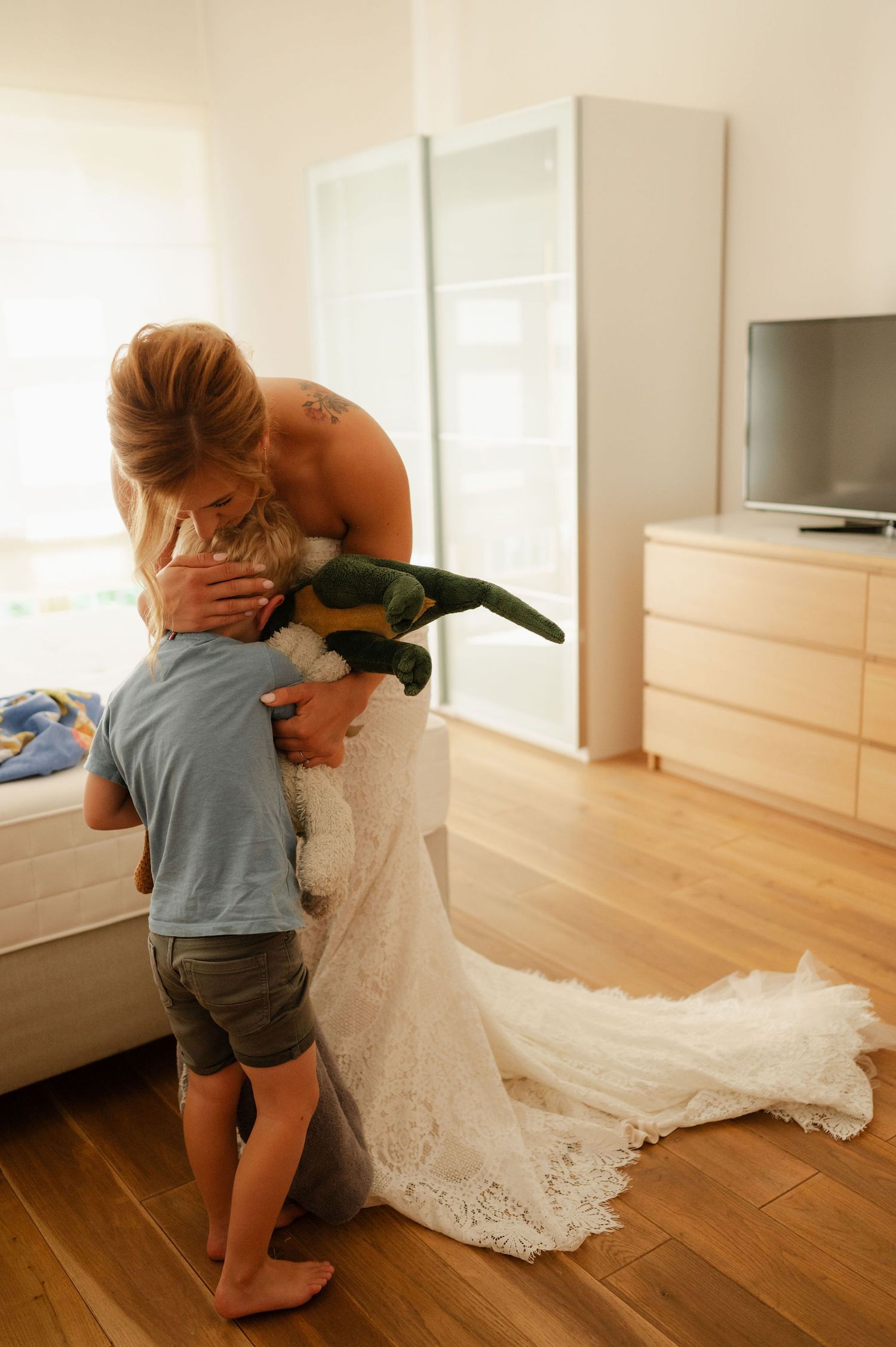 A small child in blue clothing interacts playfully with someone wearing a white wedding dress.
