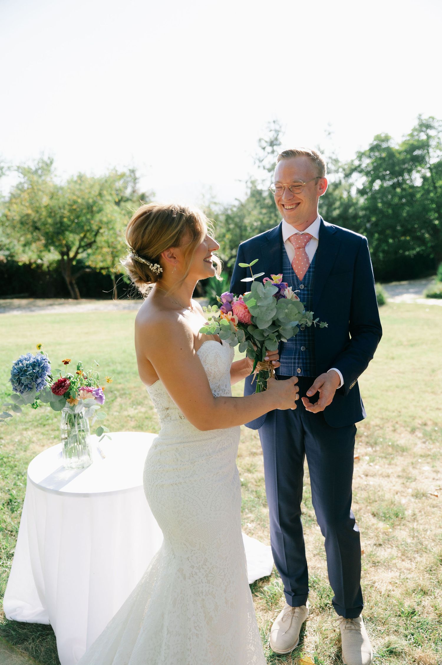 Outdoor wedding scene with white table decorations and floral arrangements in natural setting.