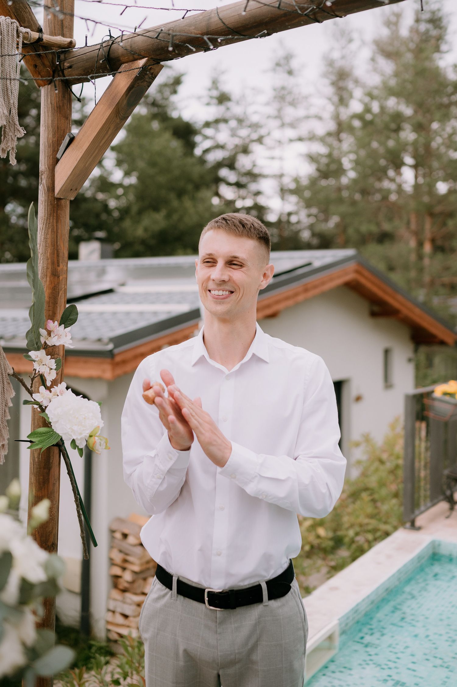 A joyful moment captured at an outdoor wedding ceremony by a pool with wooden pergola and floral decorations.