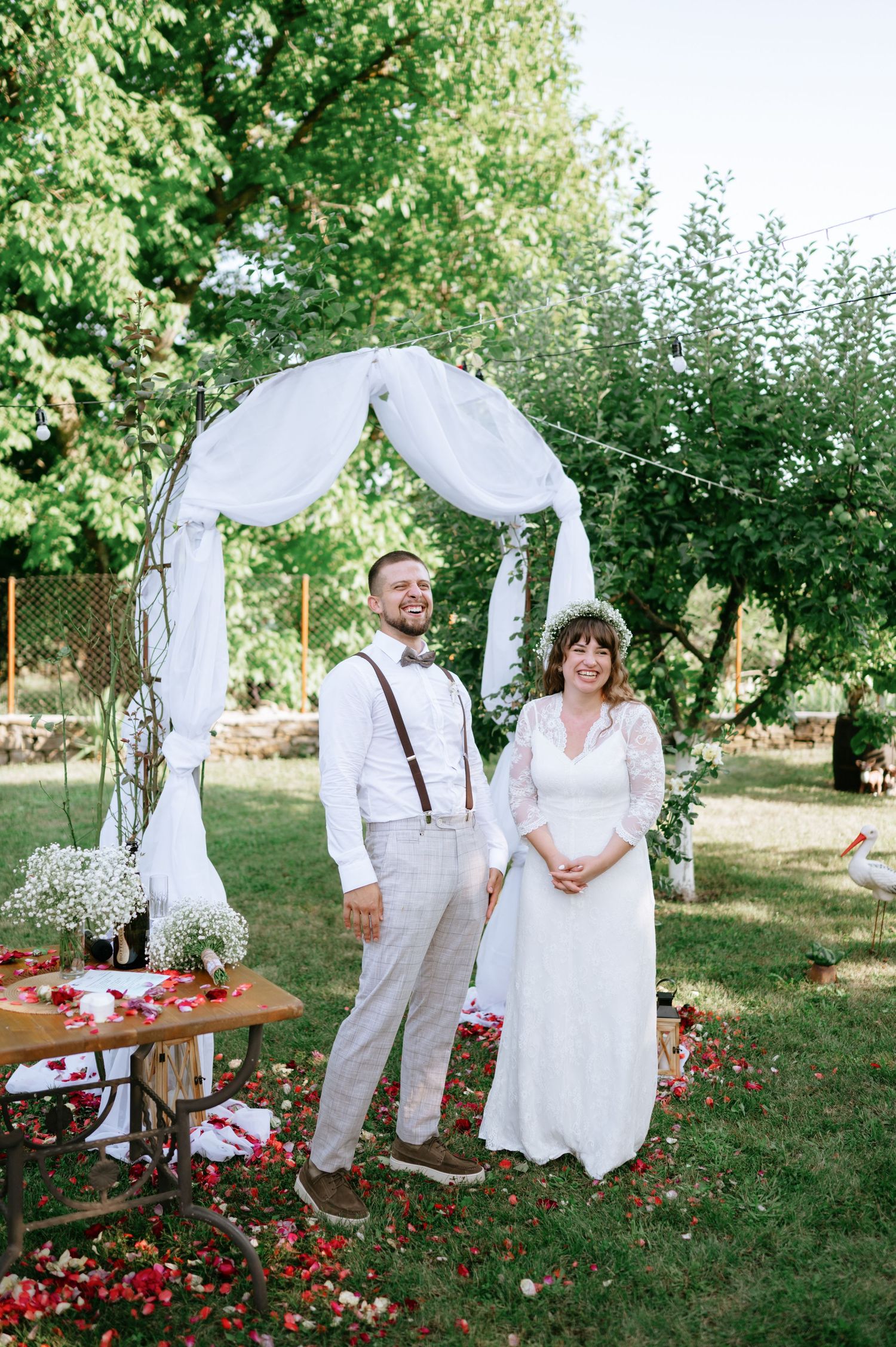 An outdoor wedding setup featuring a white fabric arch and rustic decorations in a garden setting.