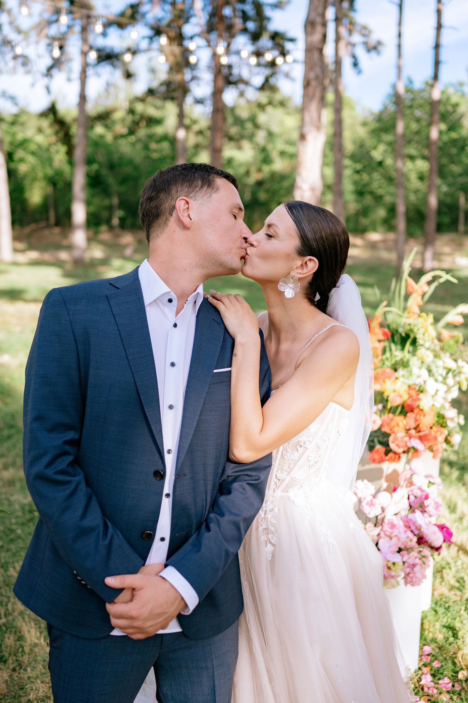 An intimate wedding moment captured in a forest setting with pink floral arrangements.