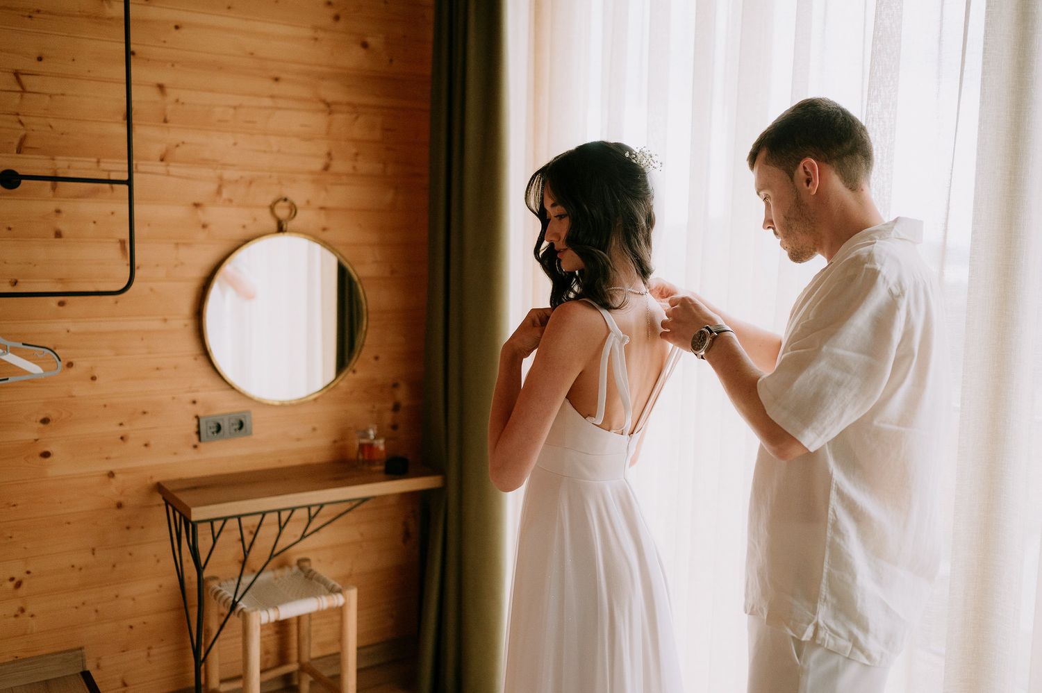Sunlit wooden interior with white curtains and elegant dress.