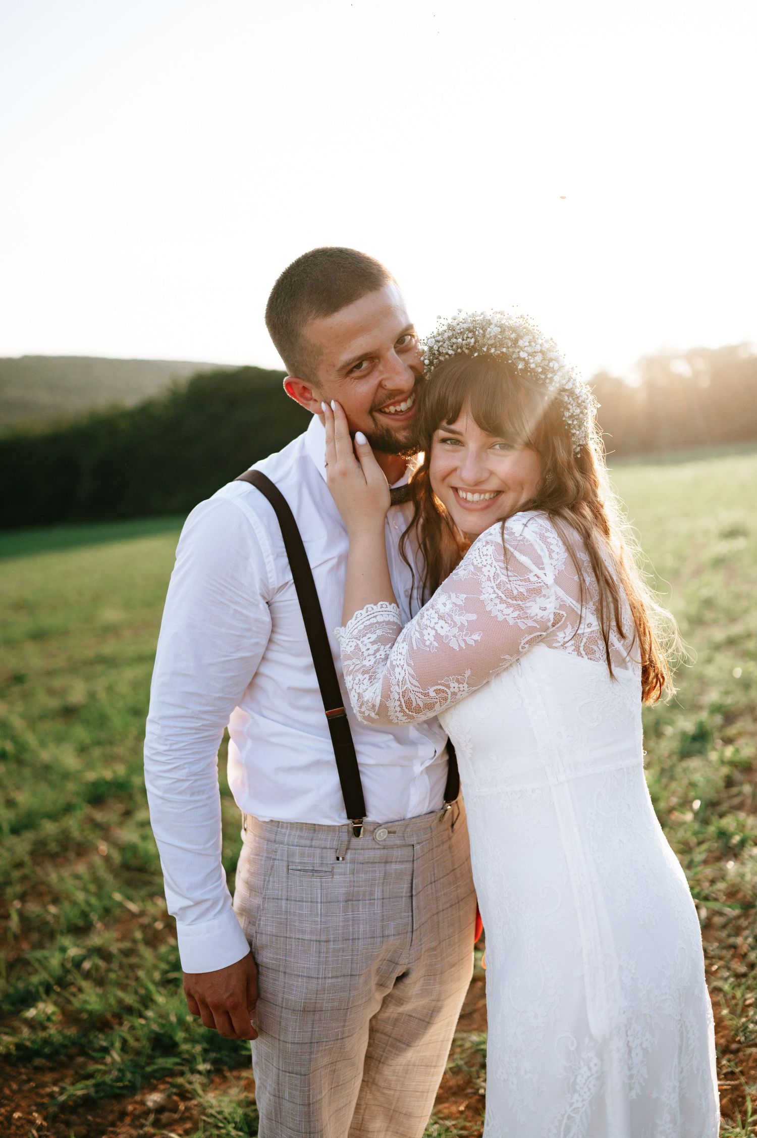 Happy newlyweds embrace in golden sunlight during outdoor wedding photoshoot.