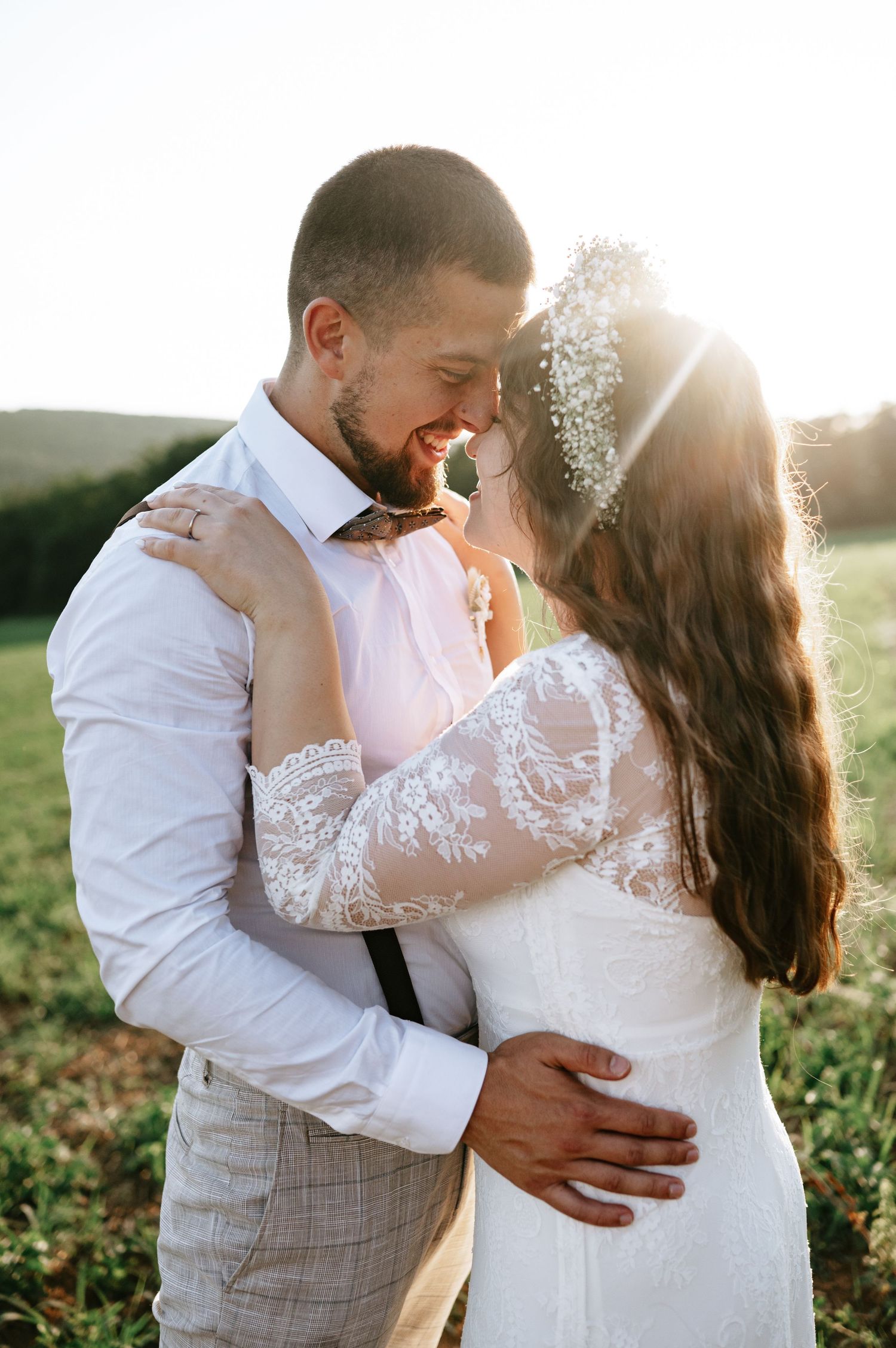A tender embrace between newlyweds in a field at sunset with soft golden light.