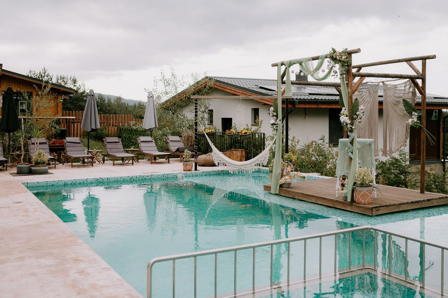 Serene poolside view with desert plants and white buildings against a cloudy sky.