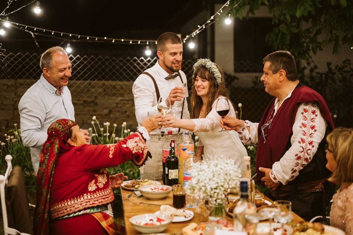 Outdoor wedding reception under string lights with guests enjoying dinner at long tables.
