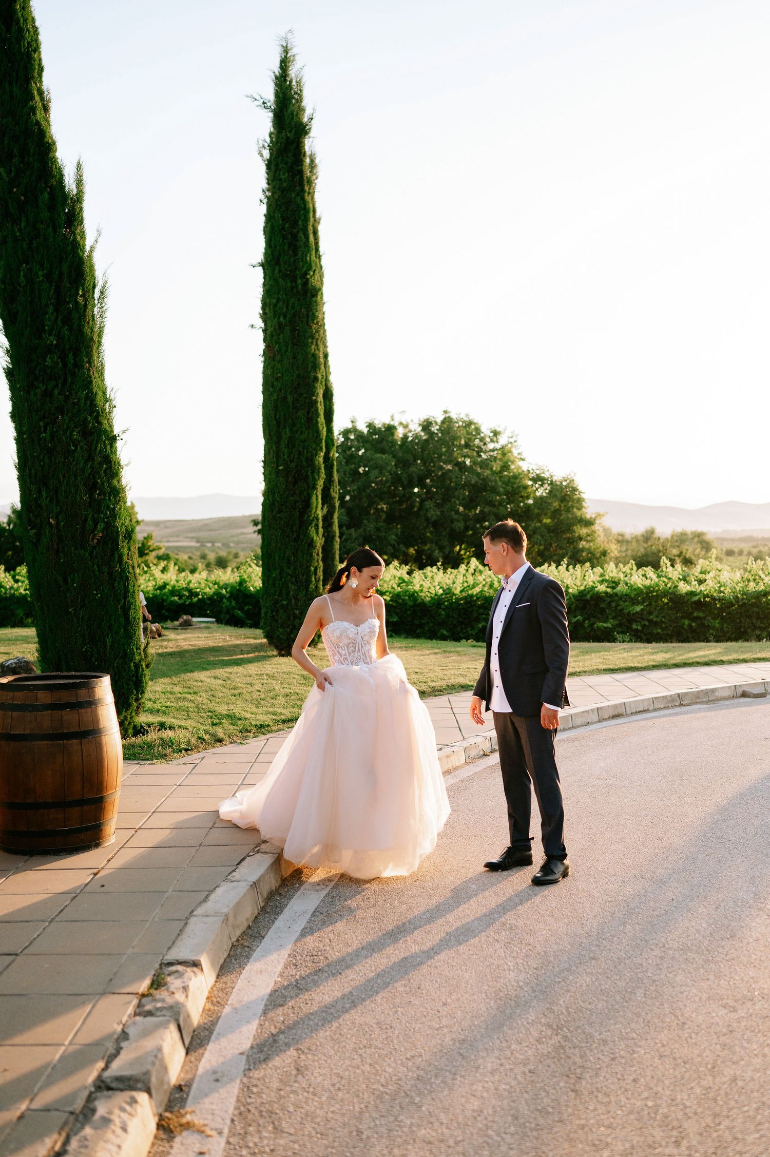 Romantic wedding couple walking along a path lined with cypress trees at golden hour.