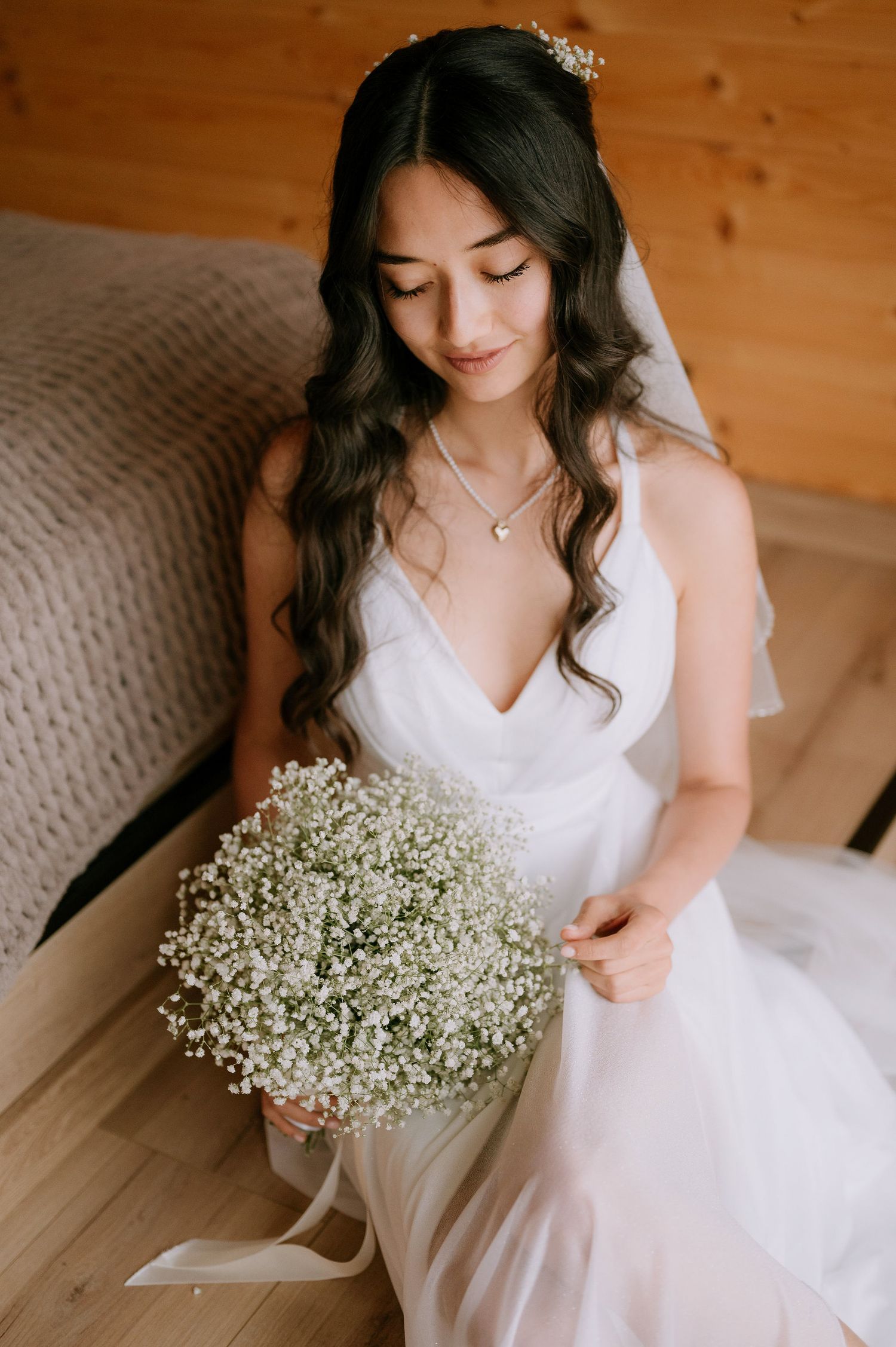 Delicate wedding photography featuring flowing white dress and baby's breath bouquet against wooden walls.