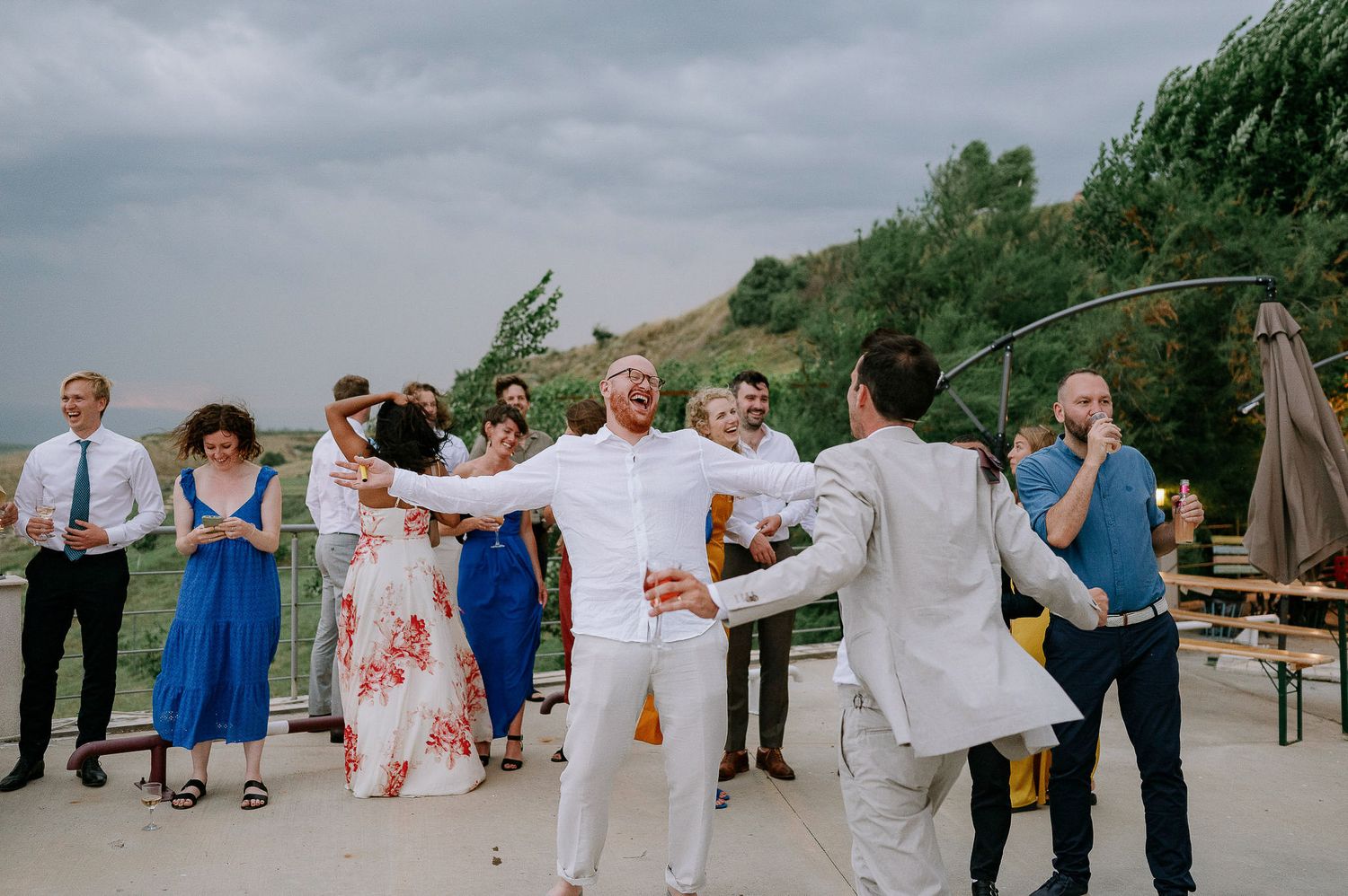 Wedding party stands in a line against dramatic cloudy sky at outdoor venue.