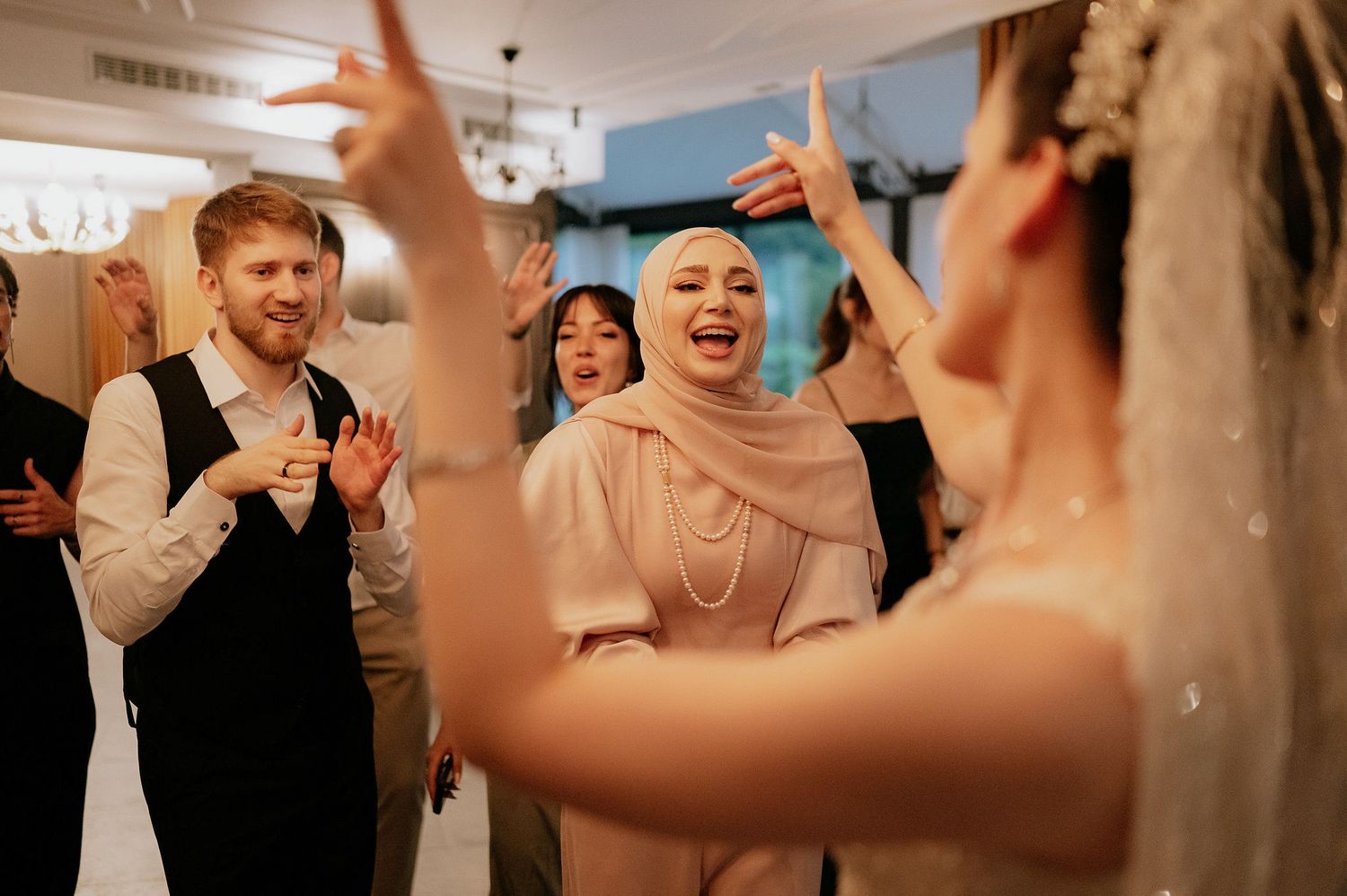 Wedding reception party with guests dancing and celebrating under indoor lighting.