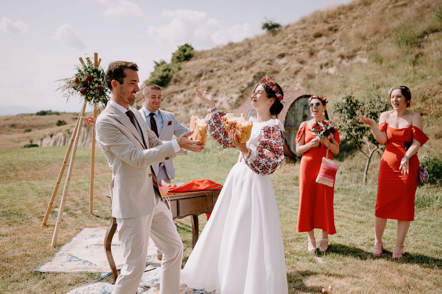Wedding celebration on hillside with coral-clad bridesmaids and floral arrangements.