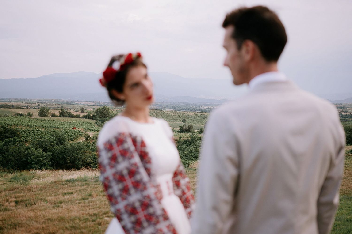 A couple shares a joyful moment on a hilltop wearing traditional folk-inspired wedding attire.