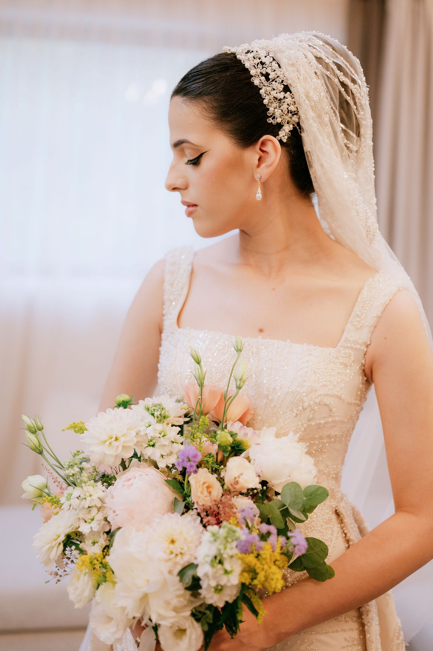 Side profile bridal portrait showcasing intricate headpiece, veil and delicate floral bouquet.