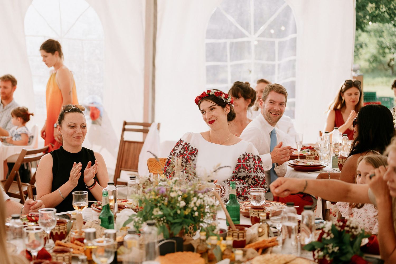 Wedding guests enjoying a meal at long tables in an elegant white tent setting.