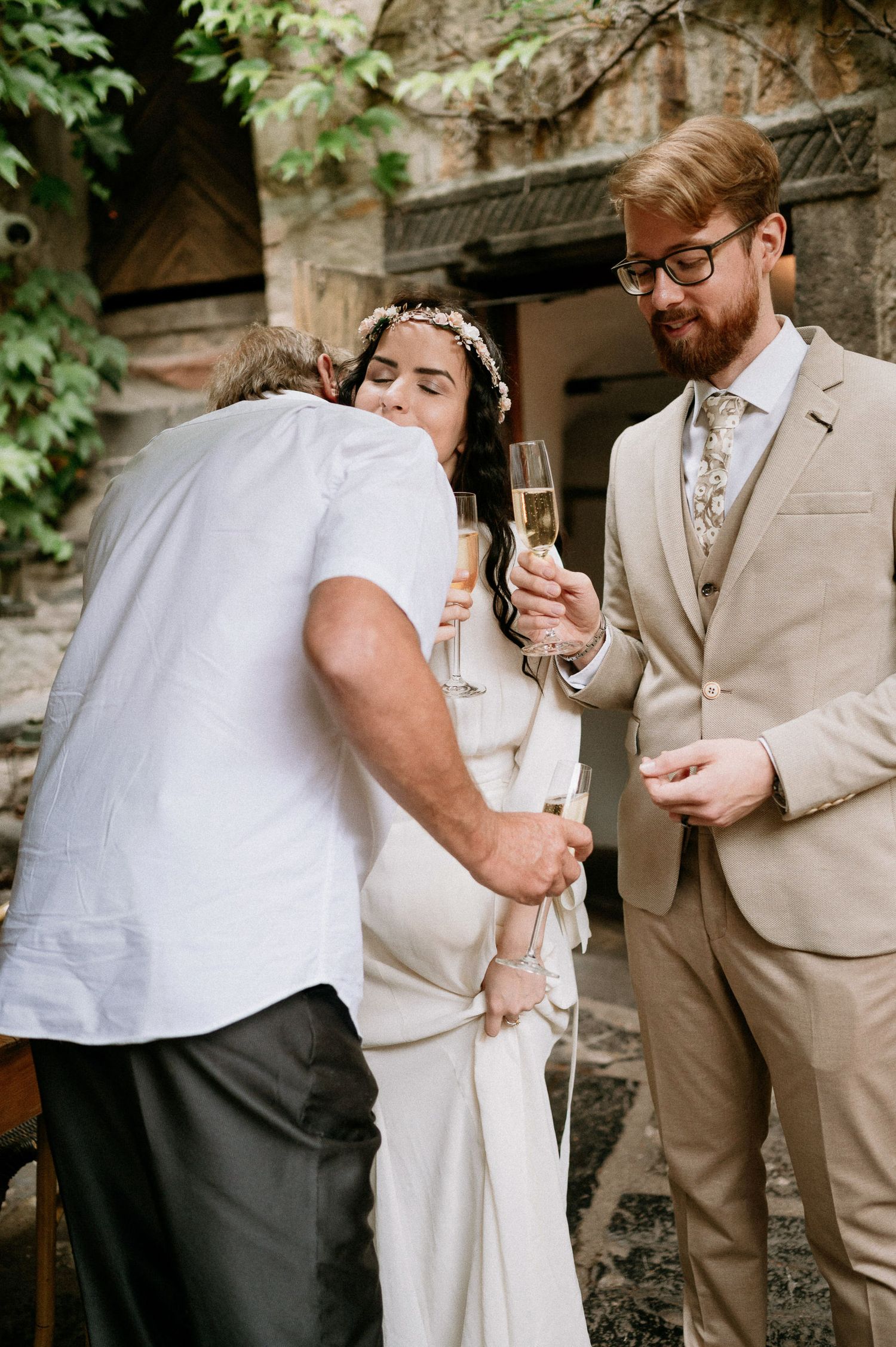 Wedding couple toasts with champagne glasses against a vintage stone backdrop.