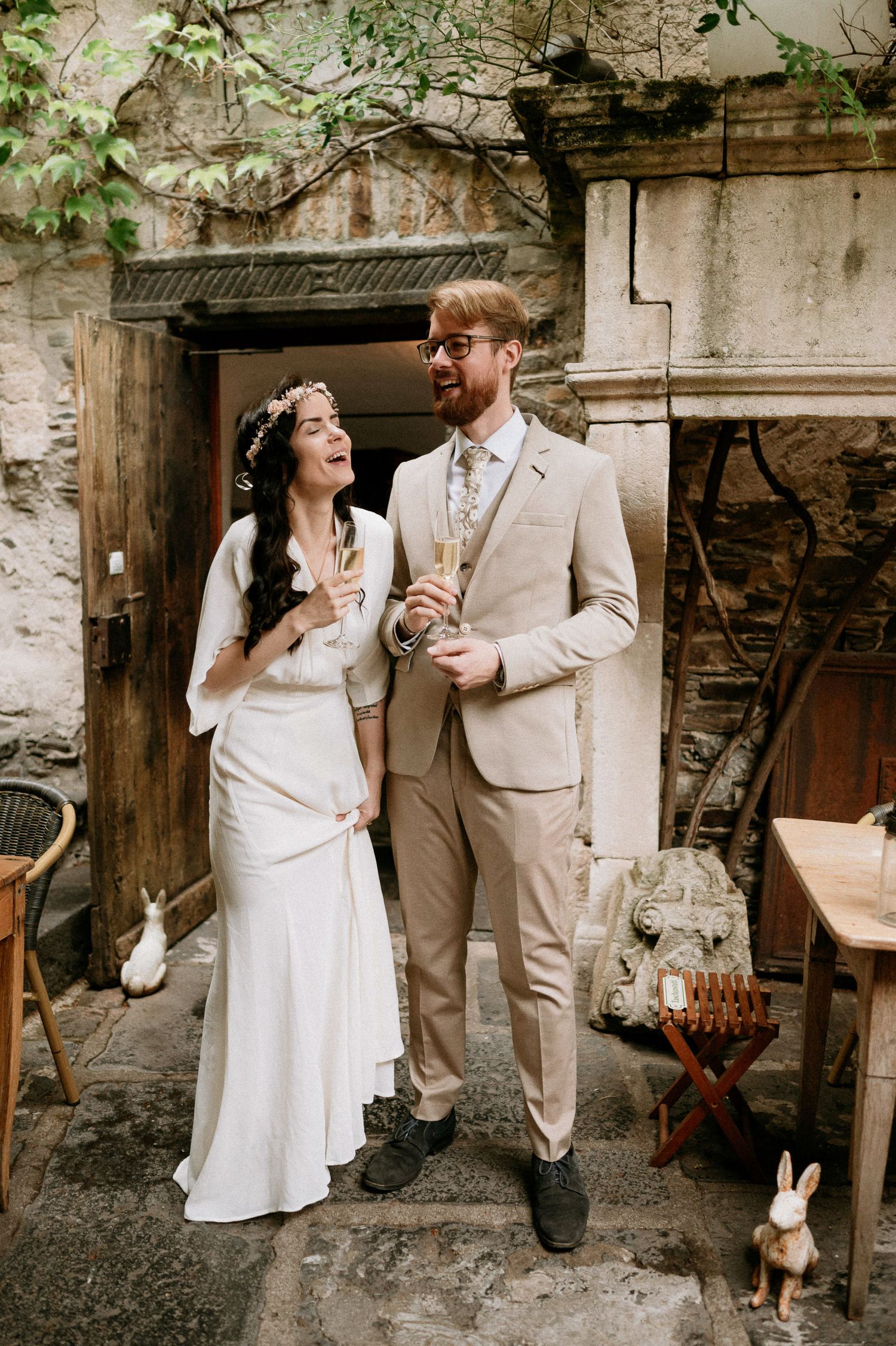 A couple shares a romantic moment in front of a rustic stone wall with climbing vines.