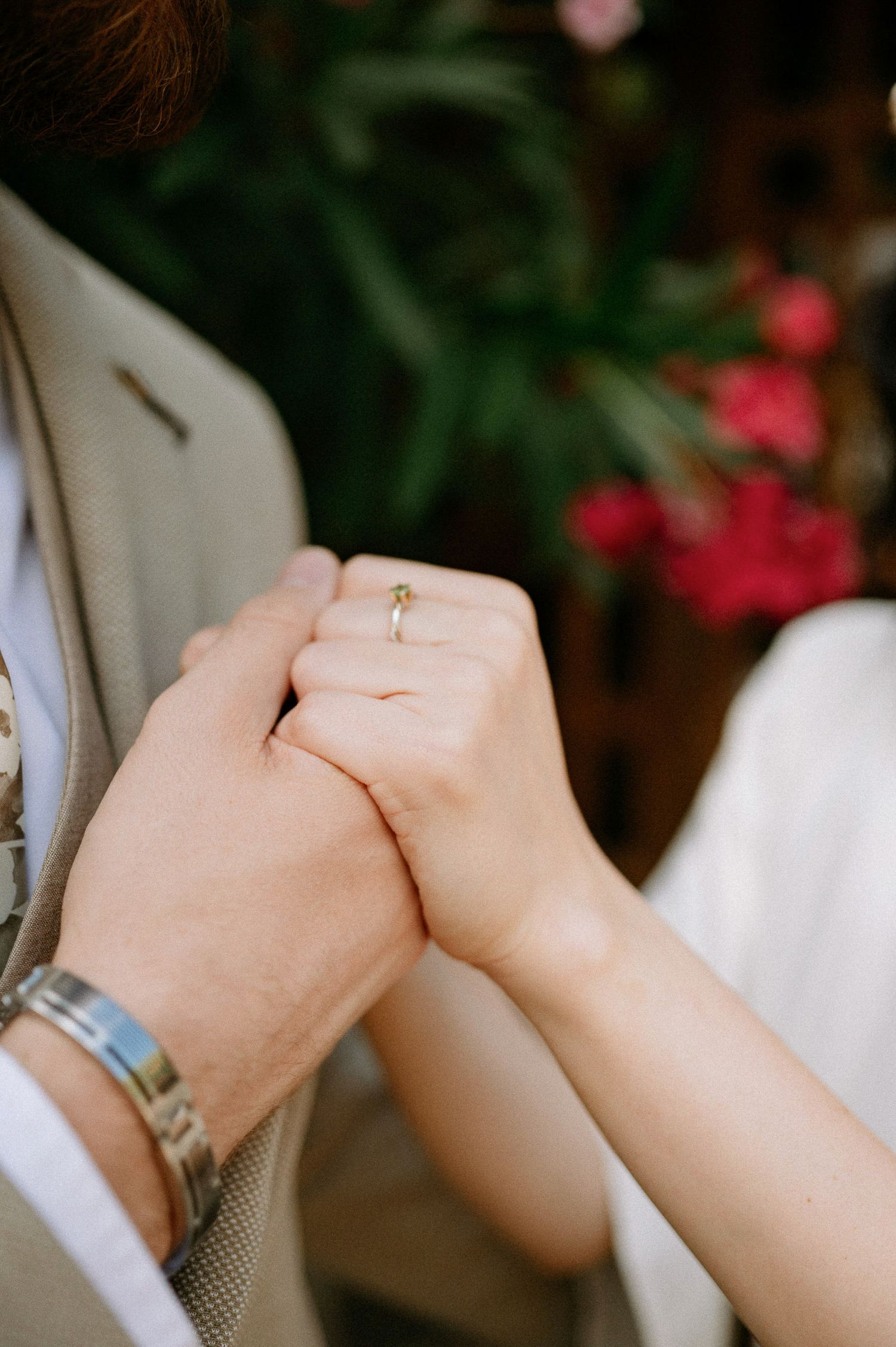 Close-up of clasped hands showing wedding rings in an intimate garden setting.