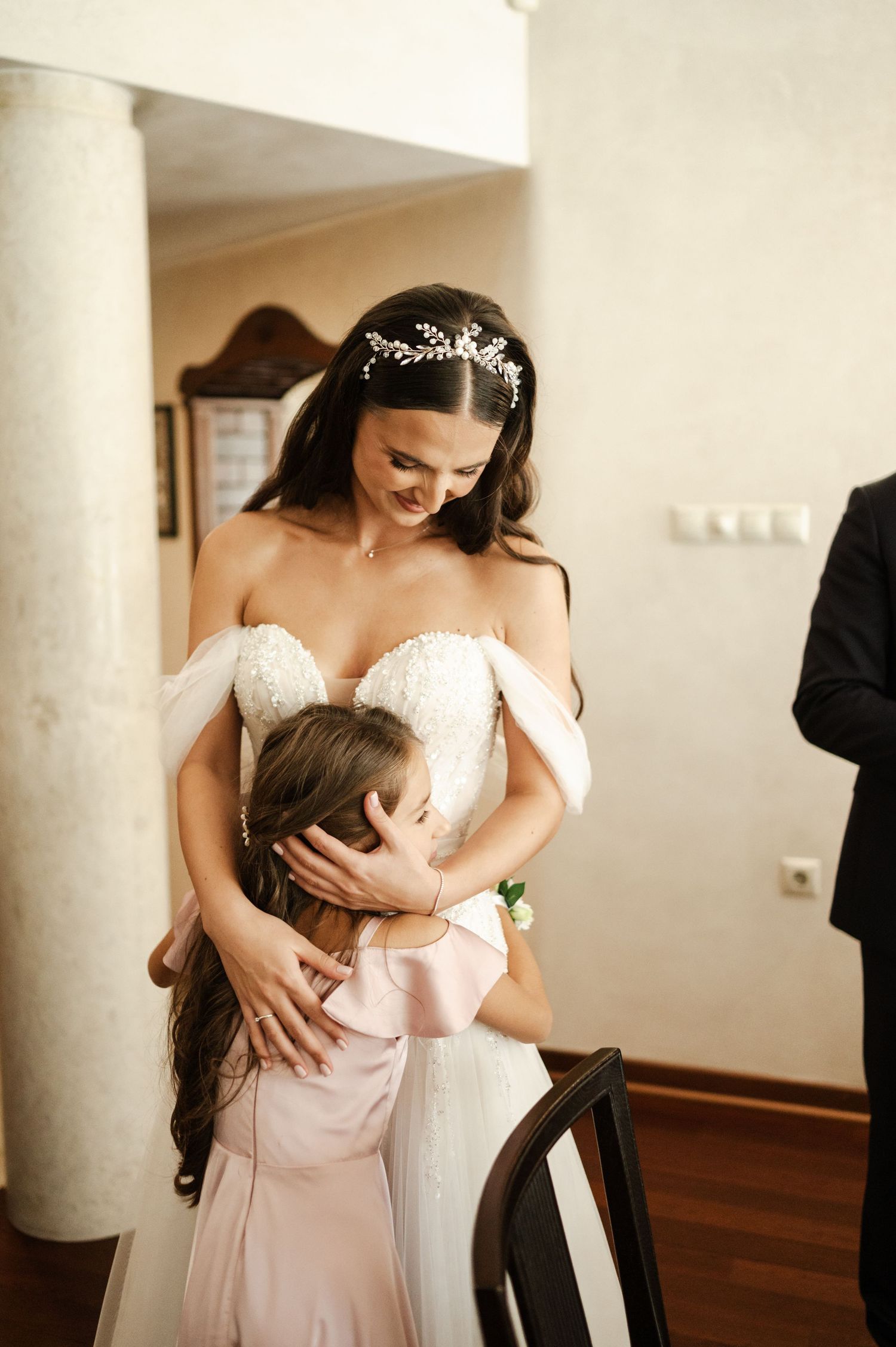 Two people share an emotional embrace in a room with classical columns.