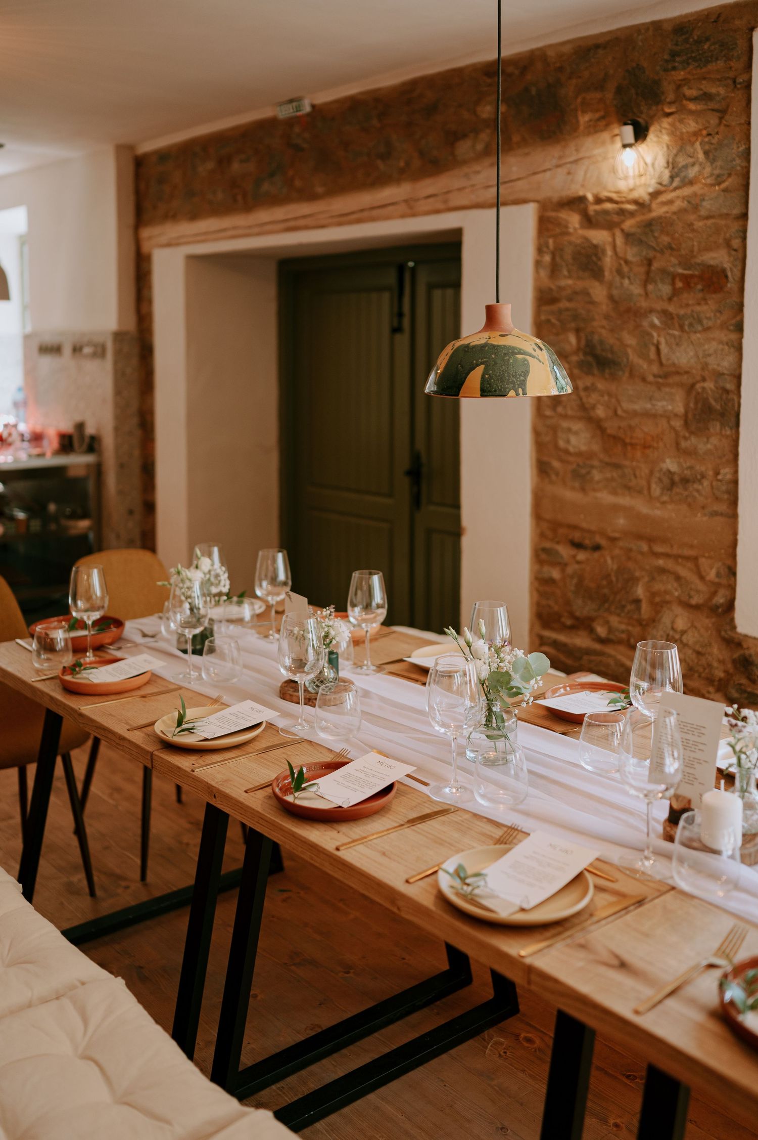 Elegant table setting with white linens and place settings in rustic dining room with stone walls.