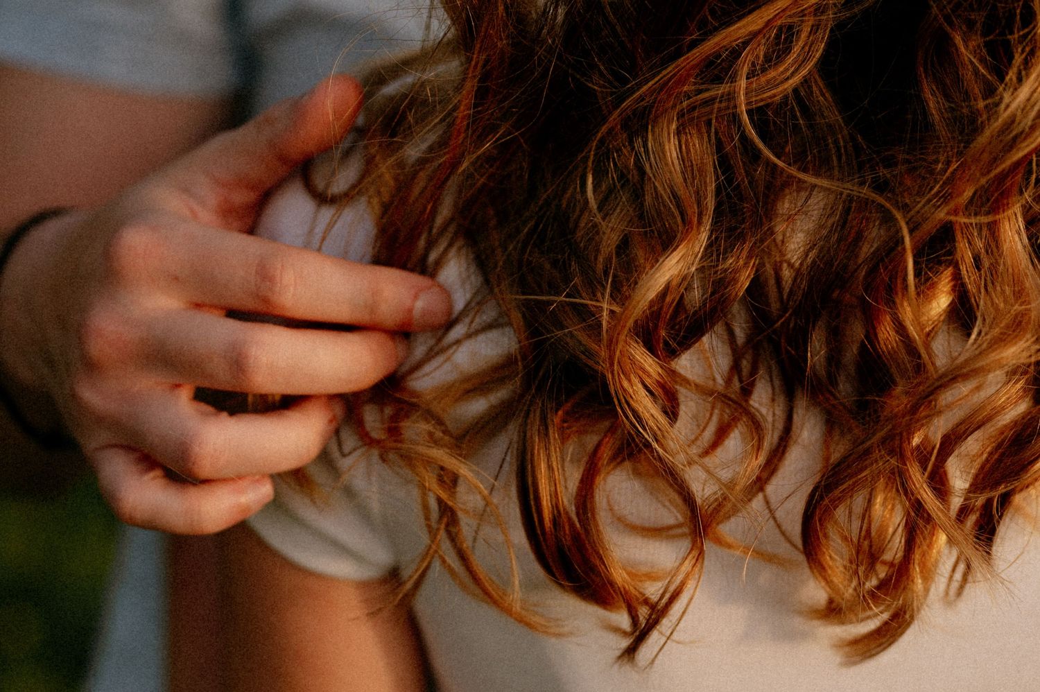 Gentle hands caressing through sun-kissed wavy hair in natural lighting.